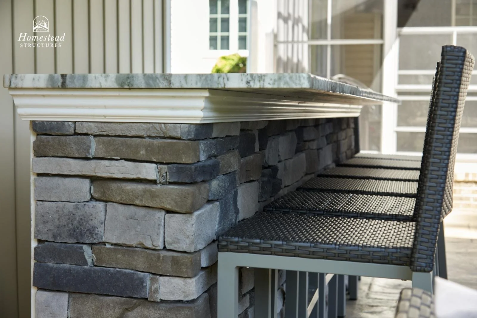 Outdoor bar or counter with a stone base and a marble top, next to a wicker chair.