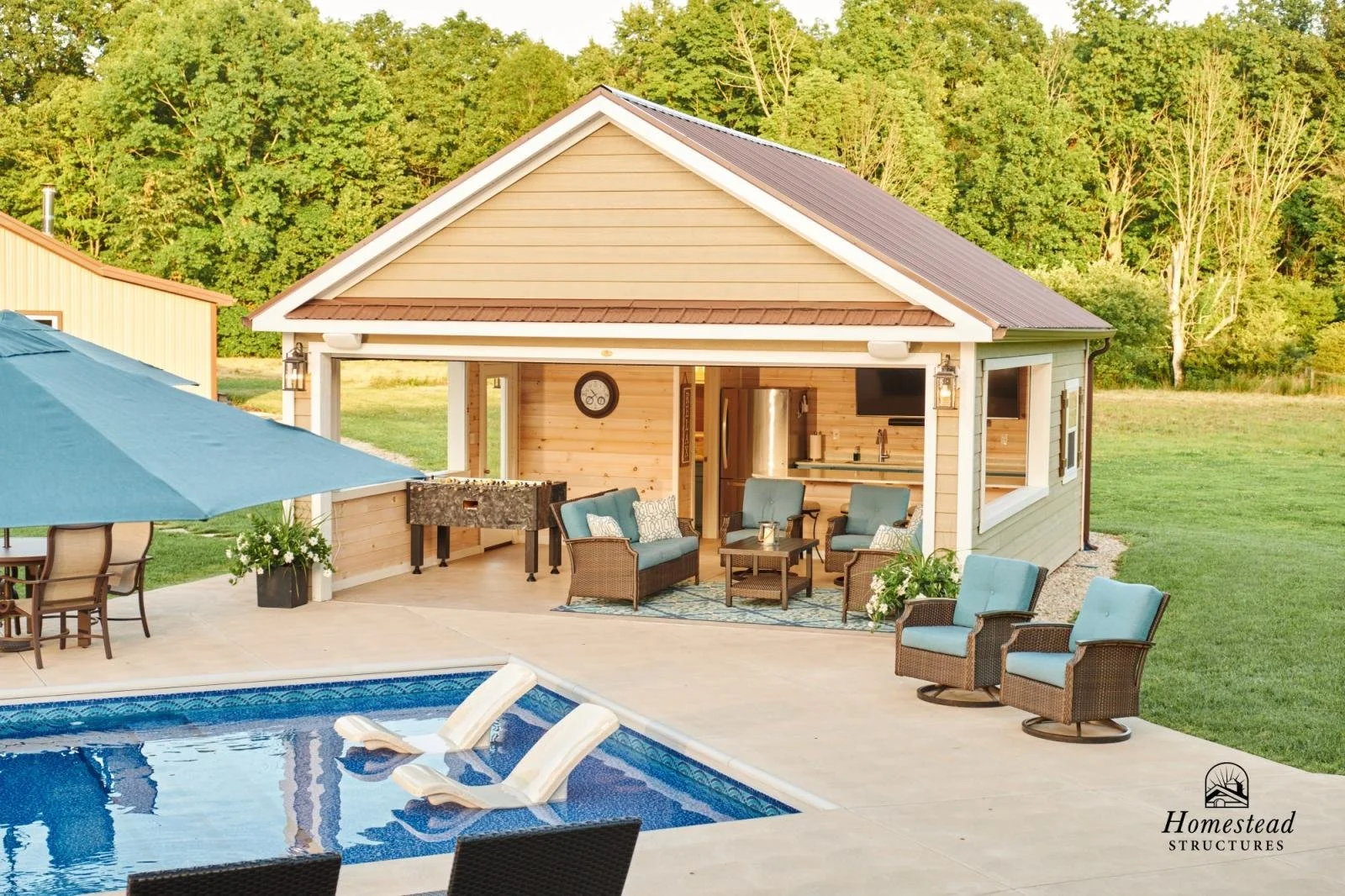 Backyard with swimming pool, outdoor seating area, and a small house or pool house in the background, surrounded by green trees.