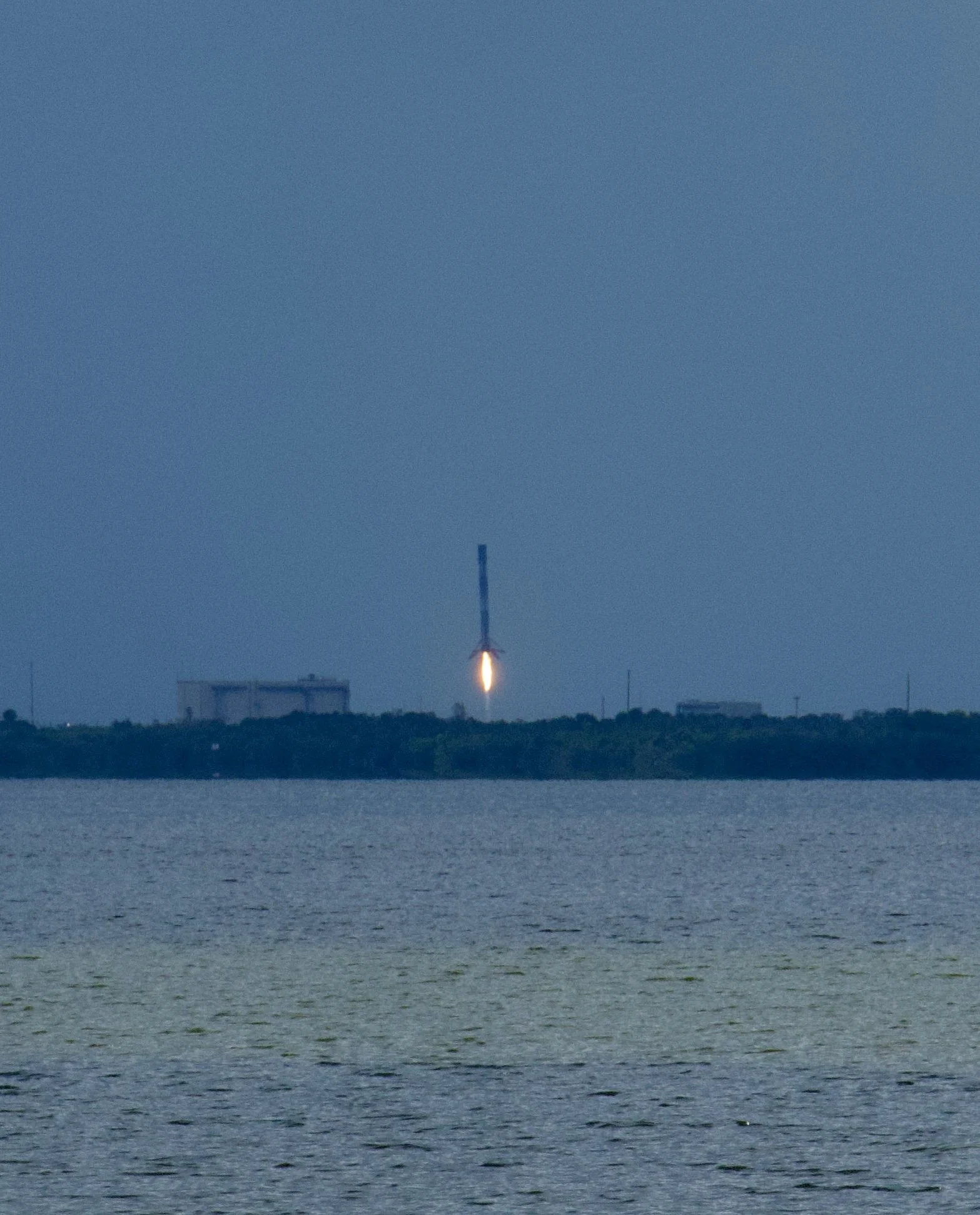 Rocket launching over water with smoke and flame, on a cloudy day.
