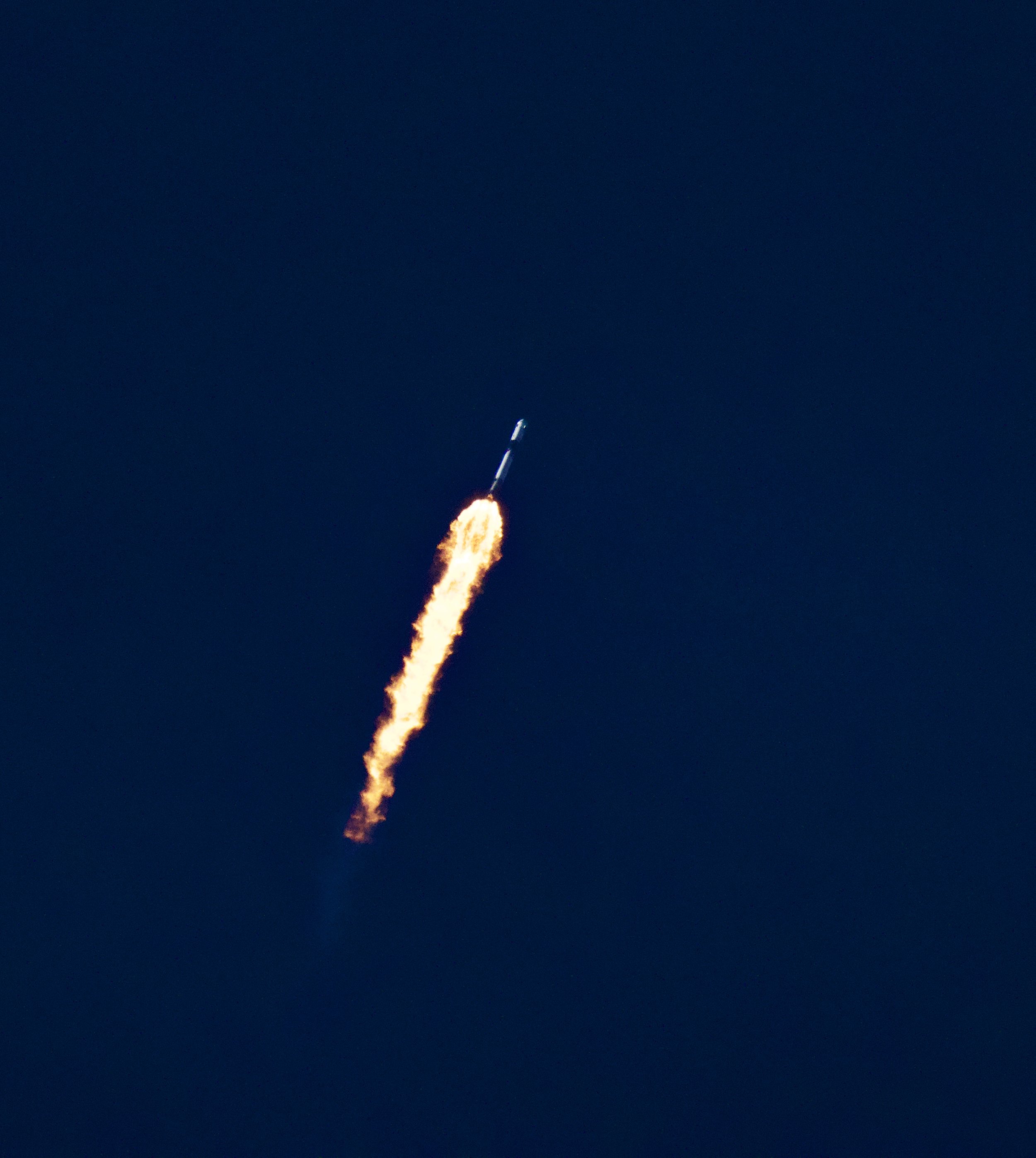A rocket leaving a fiery trail as it ascends into a dark blue sky.
