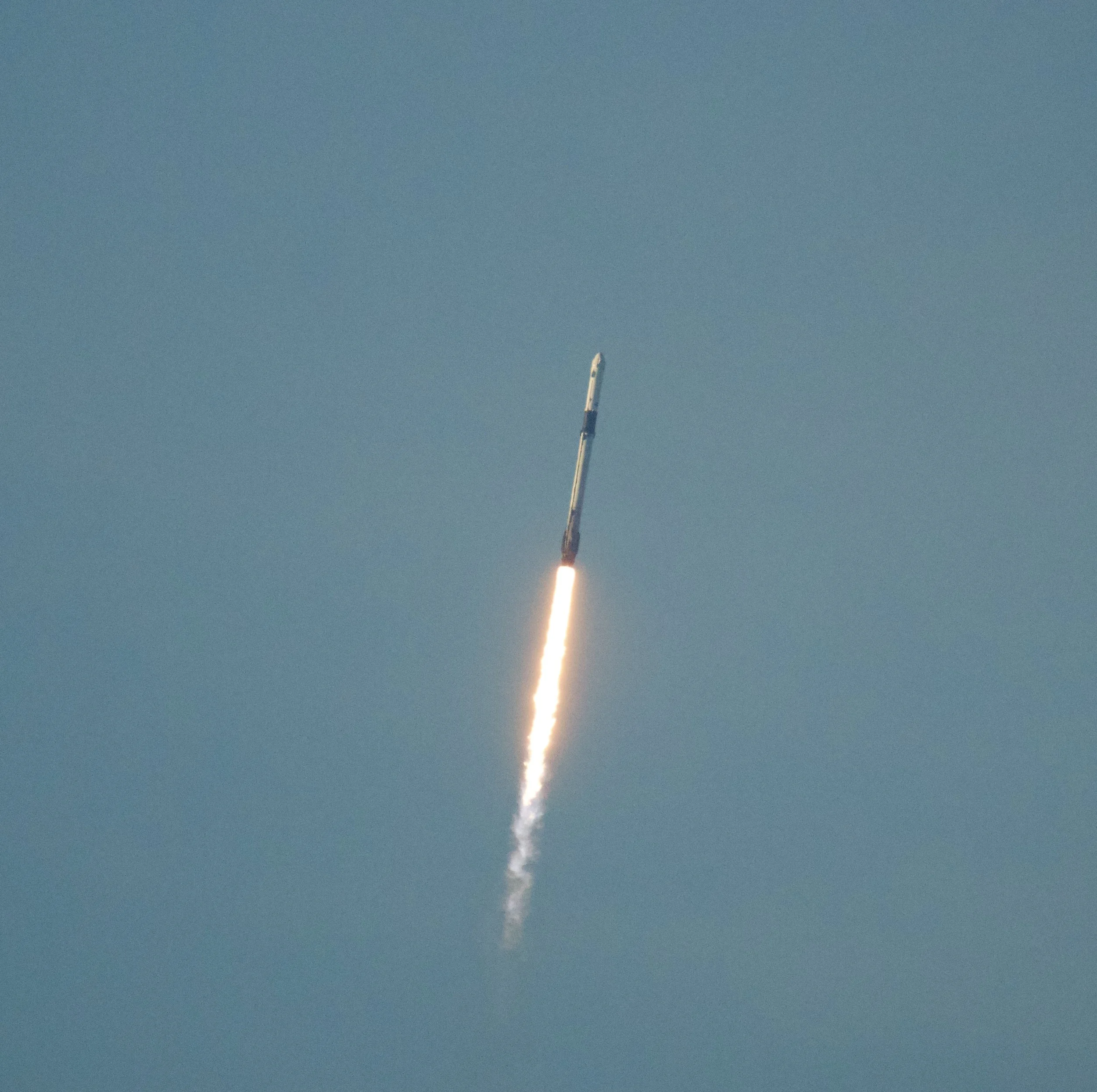 Rocket launching into the sky with a bright trail of fire and smoke against a light blue sky.