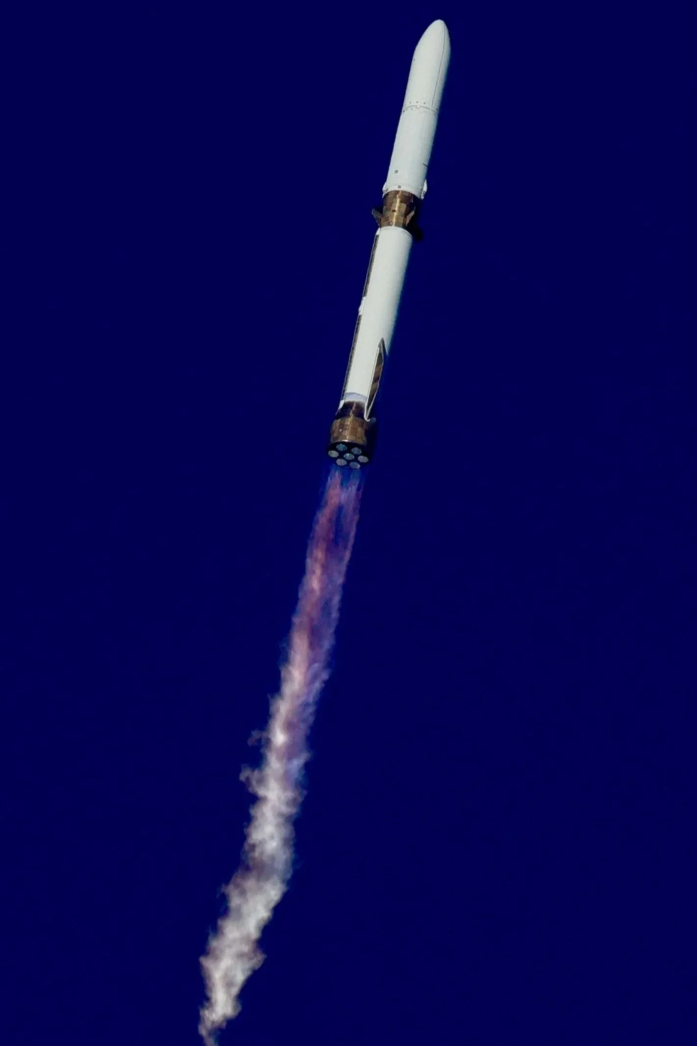 A rocket launching into the sky with smoke and fire at the base against a clear blue sky.