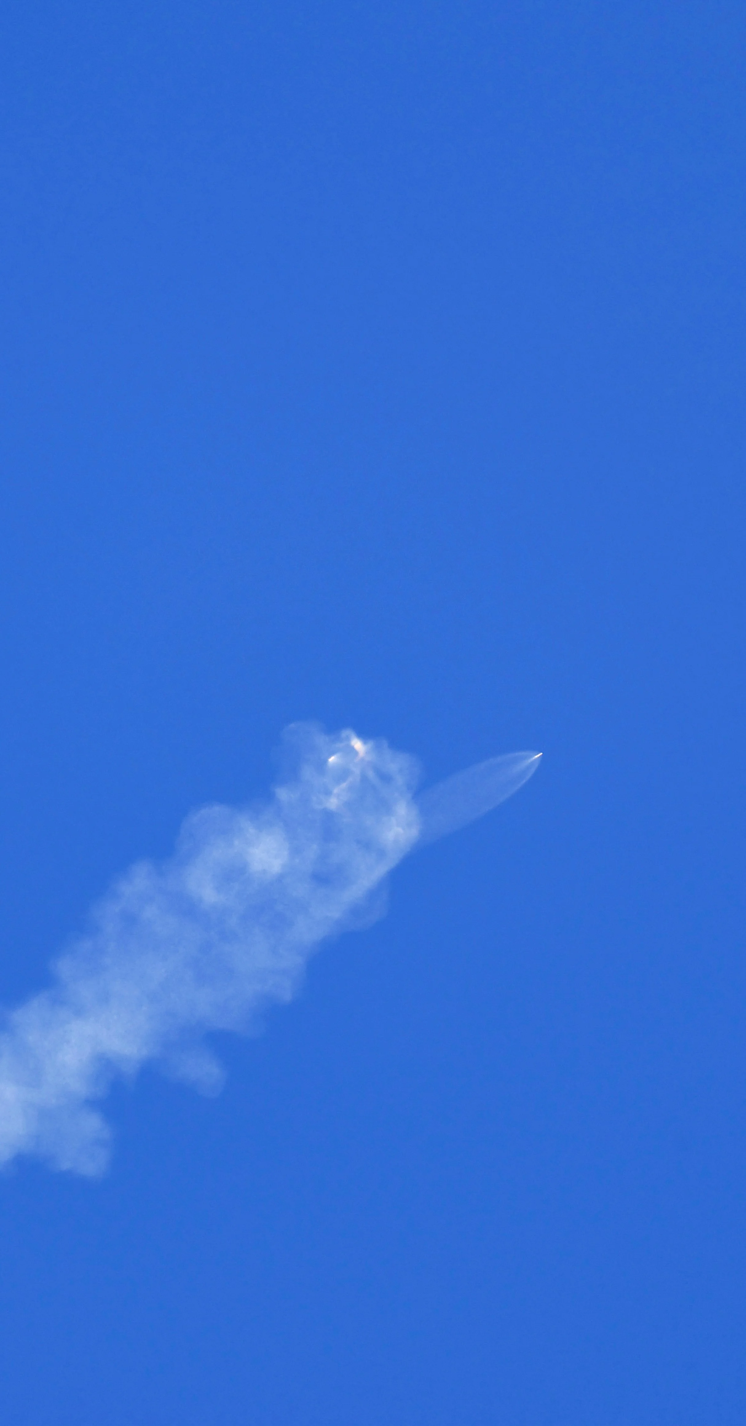 A rocket launching into a clear blue sky, with a trail of white smoke behind it.