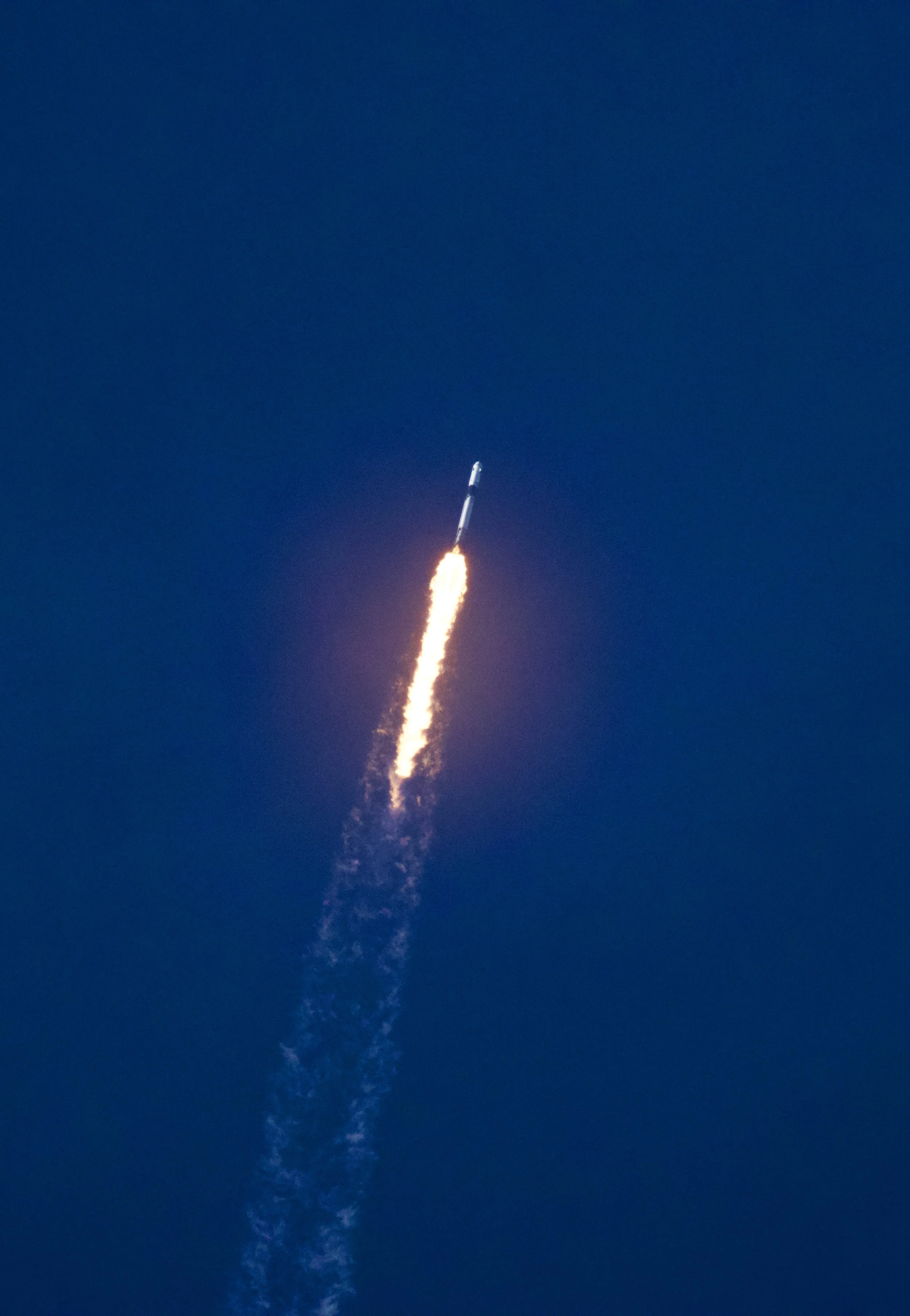 A rocket launching into a clear blue sky with a trail of flames and smoke.