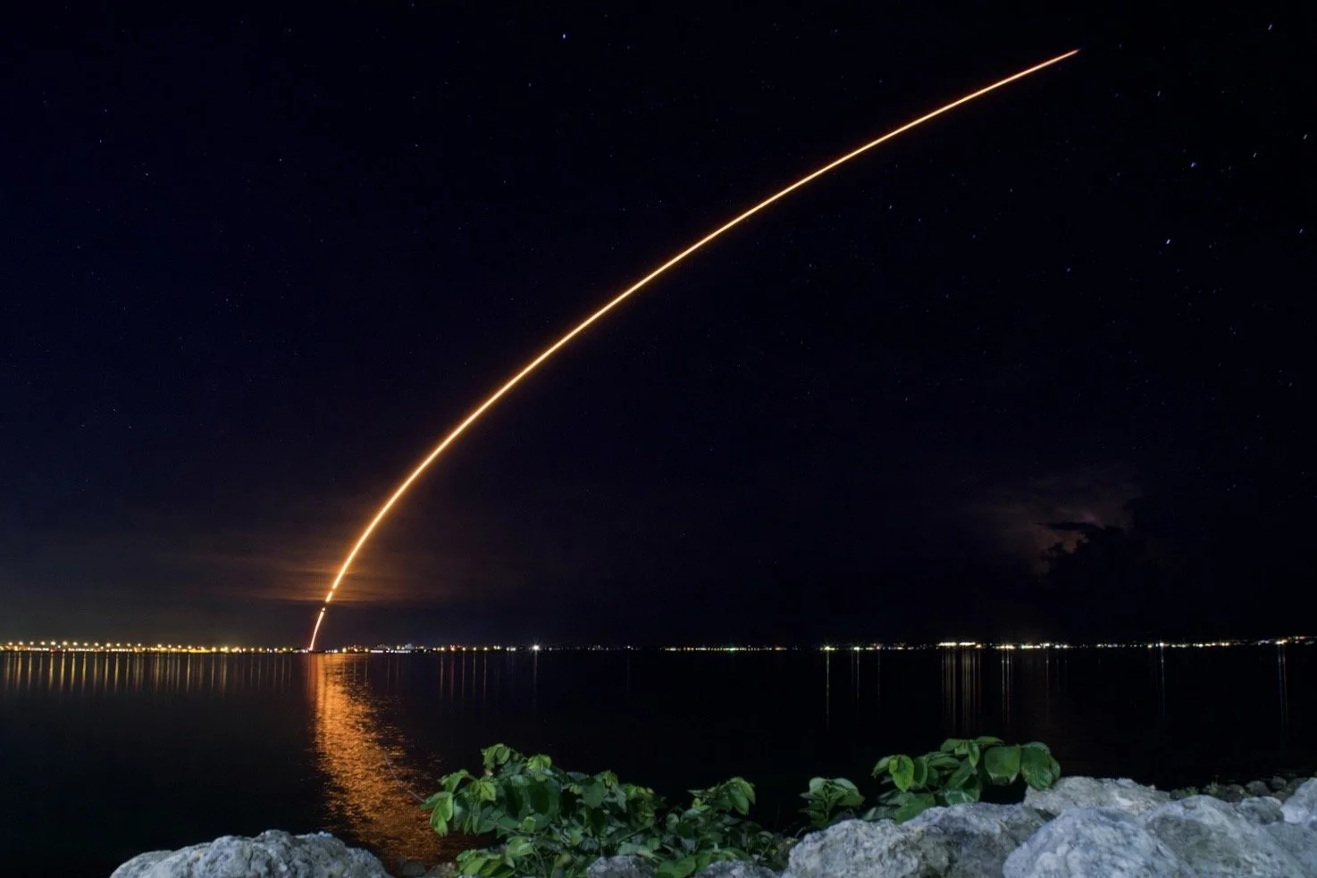 Night rocket launch streak over water