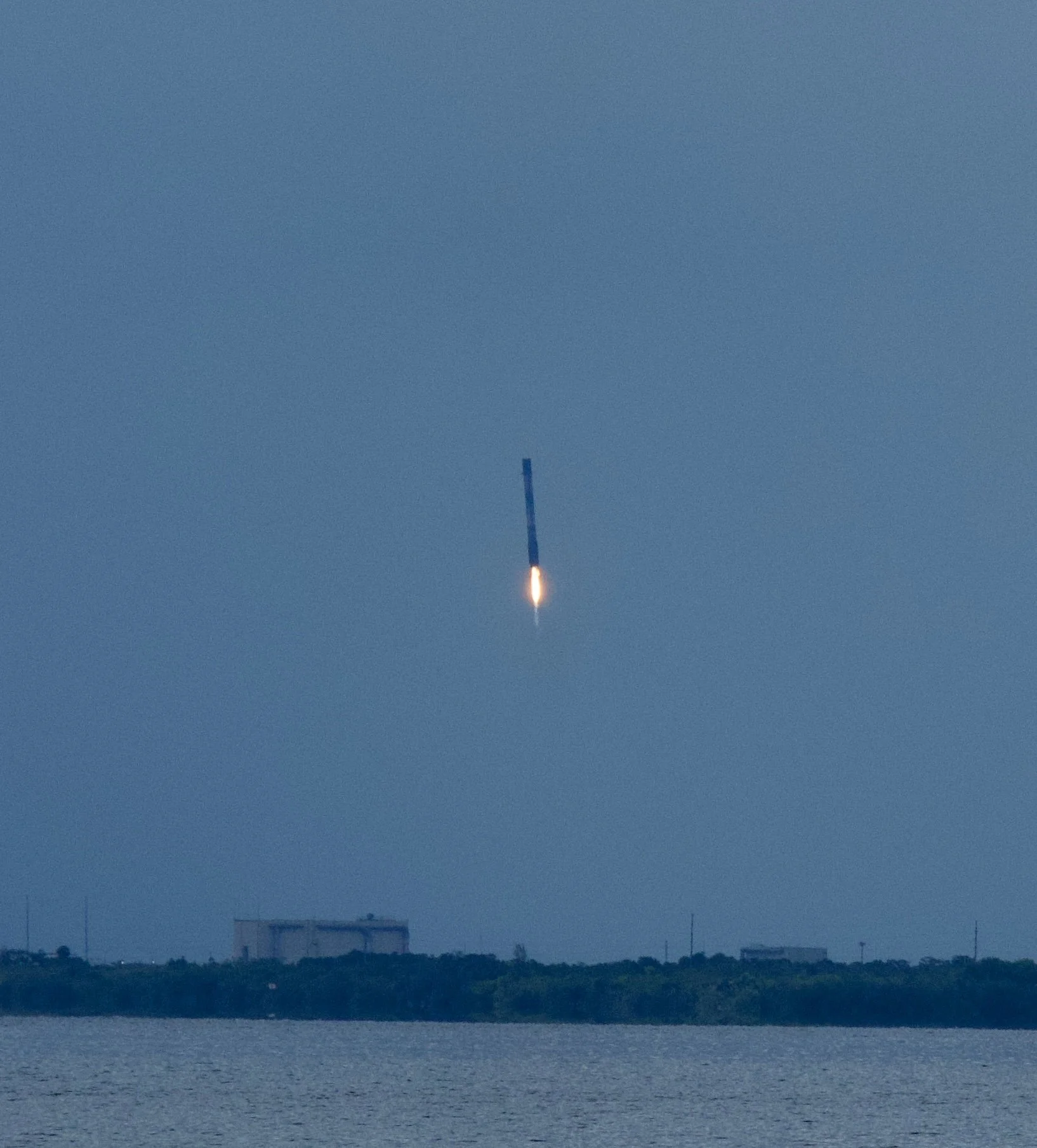 A rocket launching into the sky over a body of water, with a clear blue sky background.