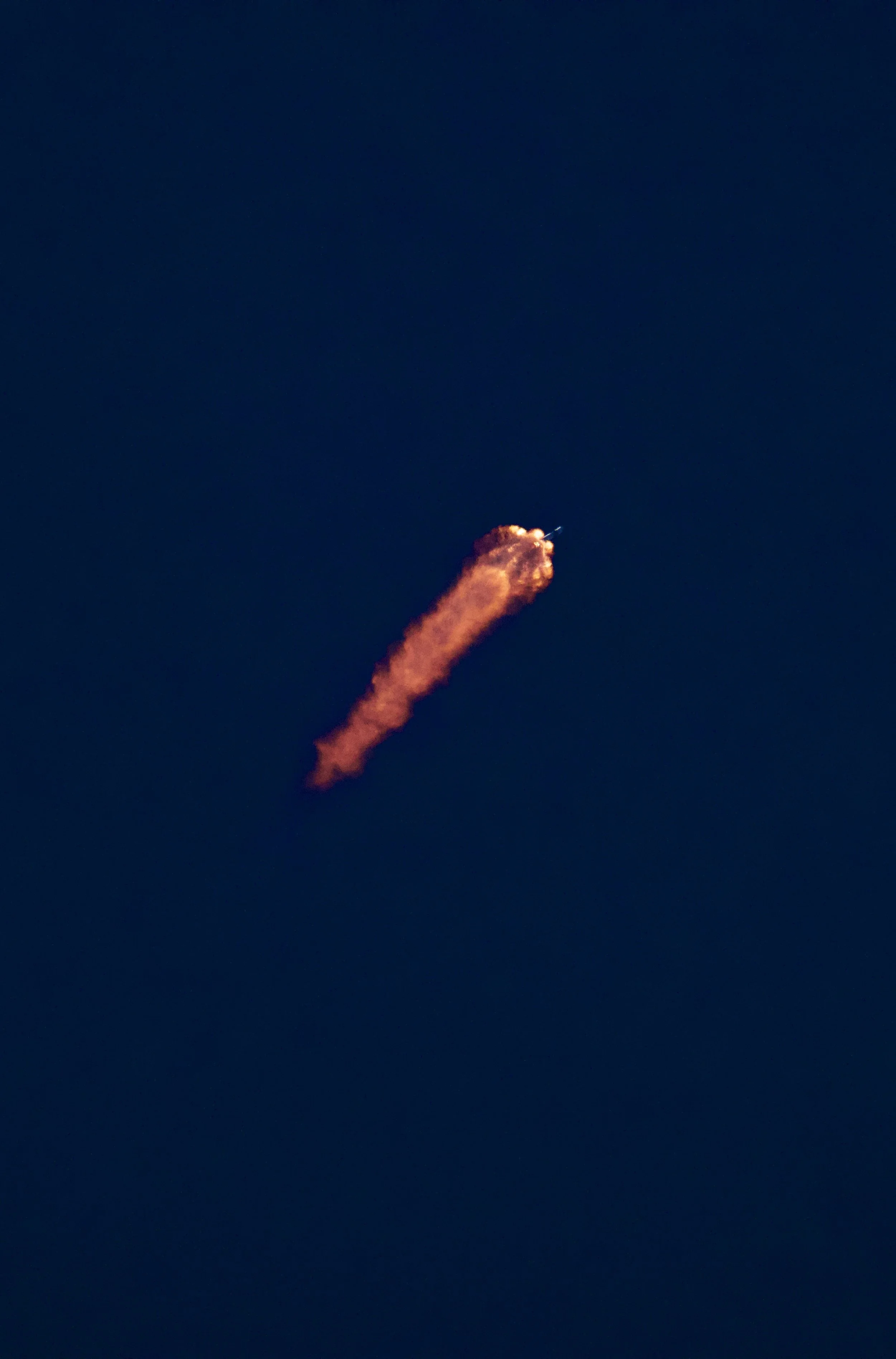 A rocket launching into the sky, leaving a trail of orange and pink flames against a dark blue evening sky.