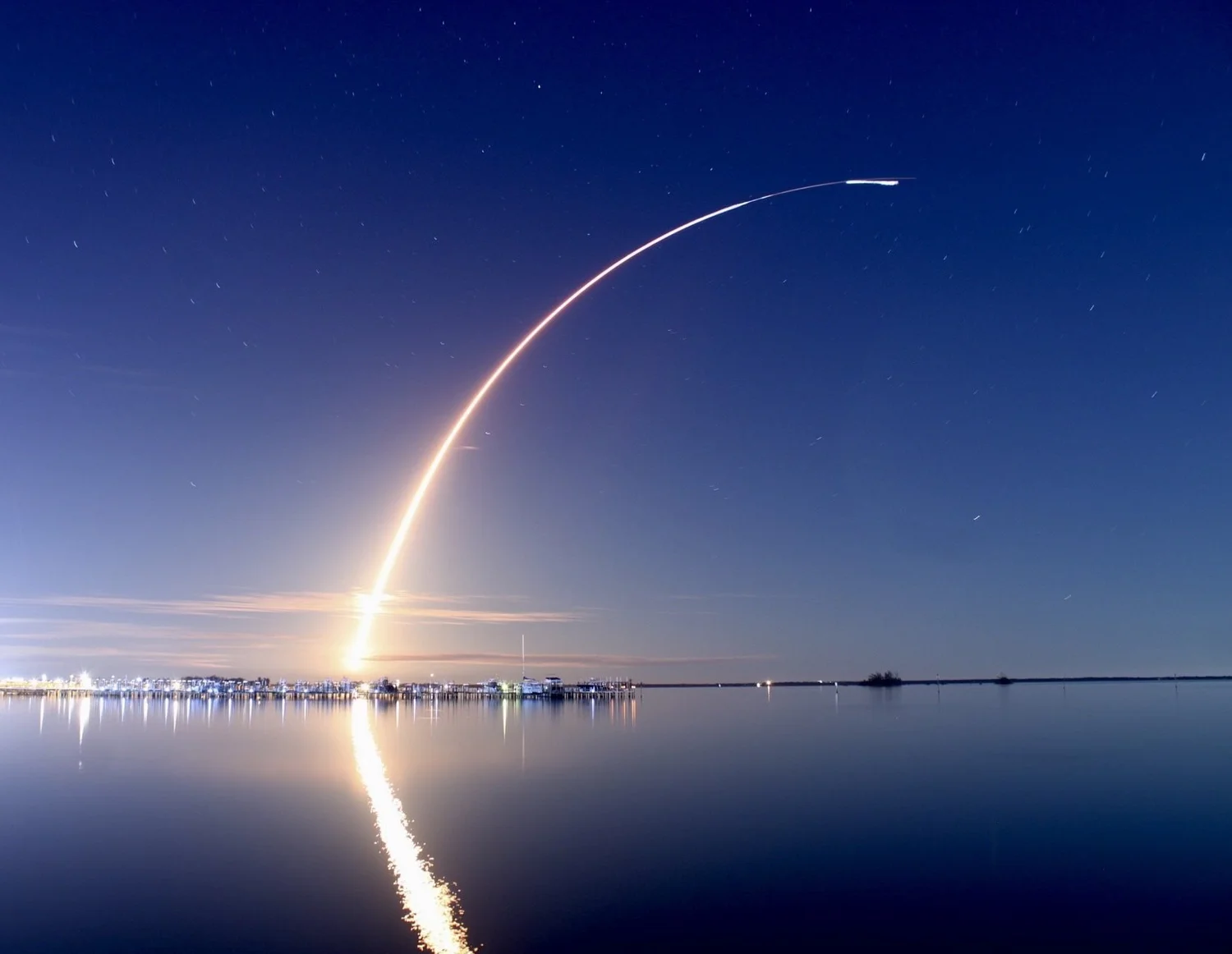Rocket launch streak reflecting over water at night