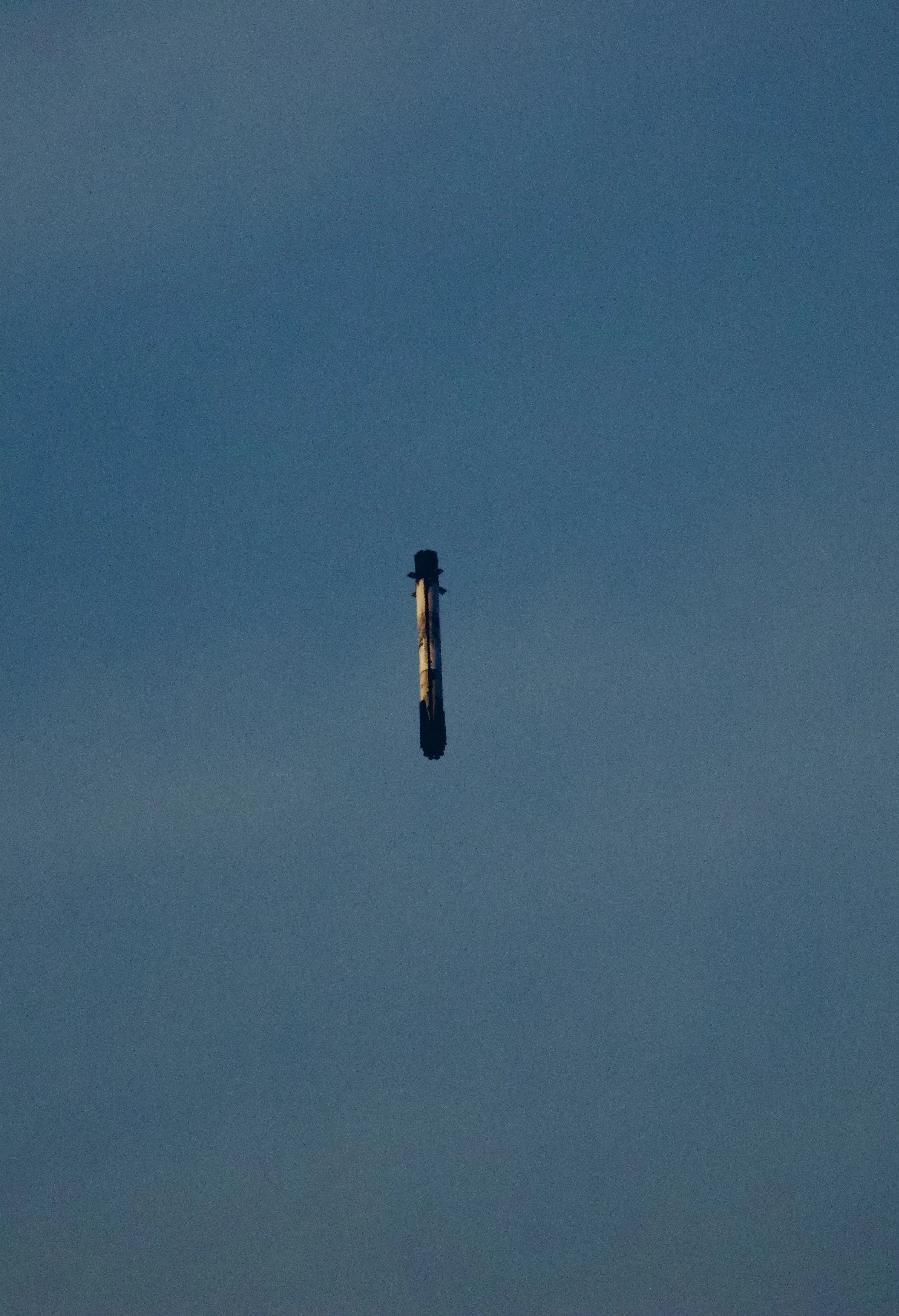 A small object, possibly a drone or drone part, is suspended in the clear blue sky.