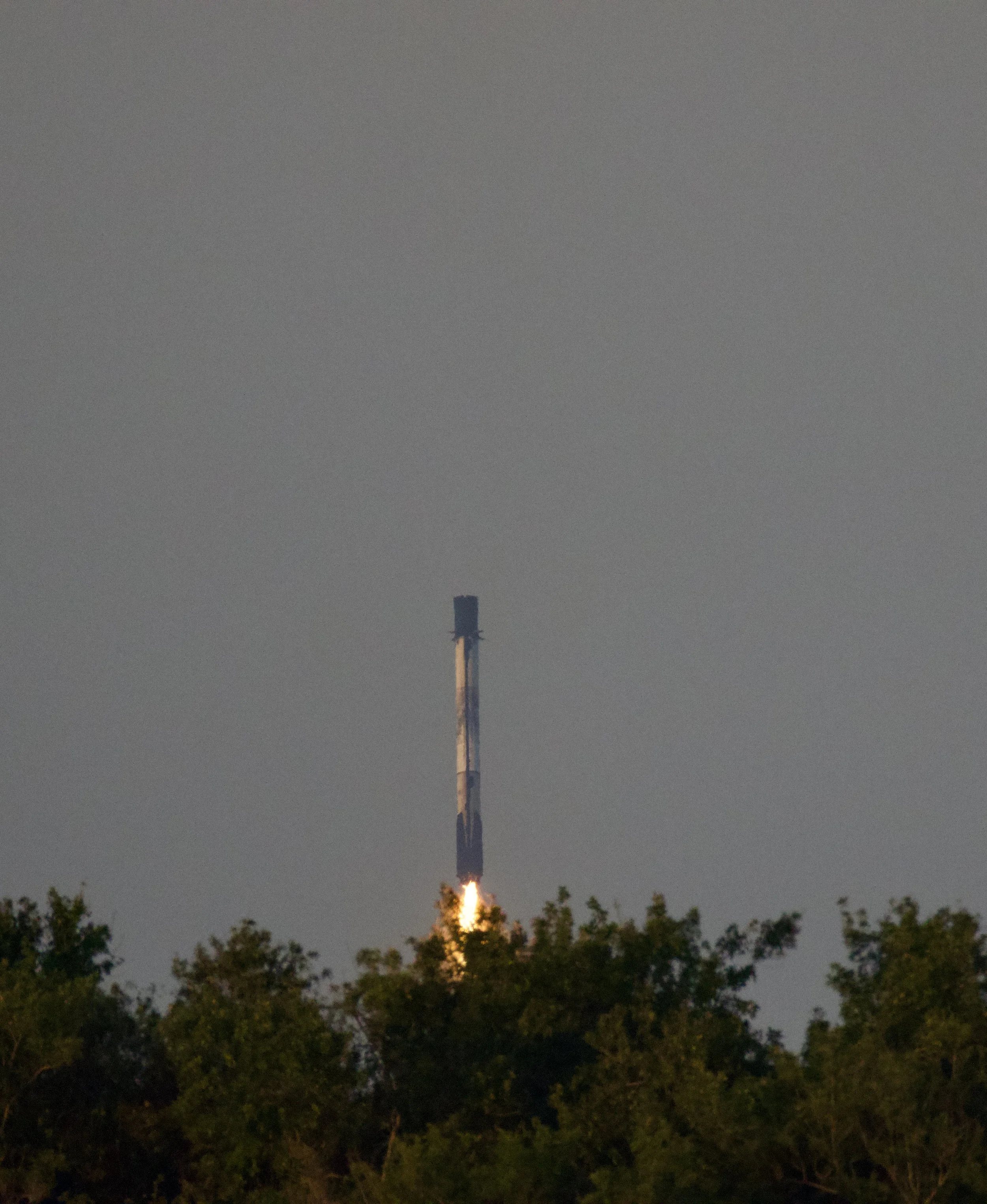 A rocket launching from a forested area with a trail of flames and smoke.