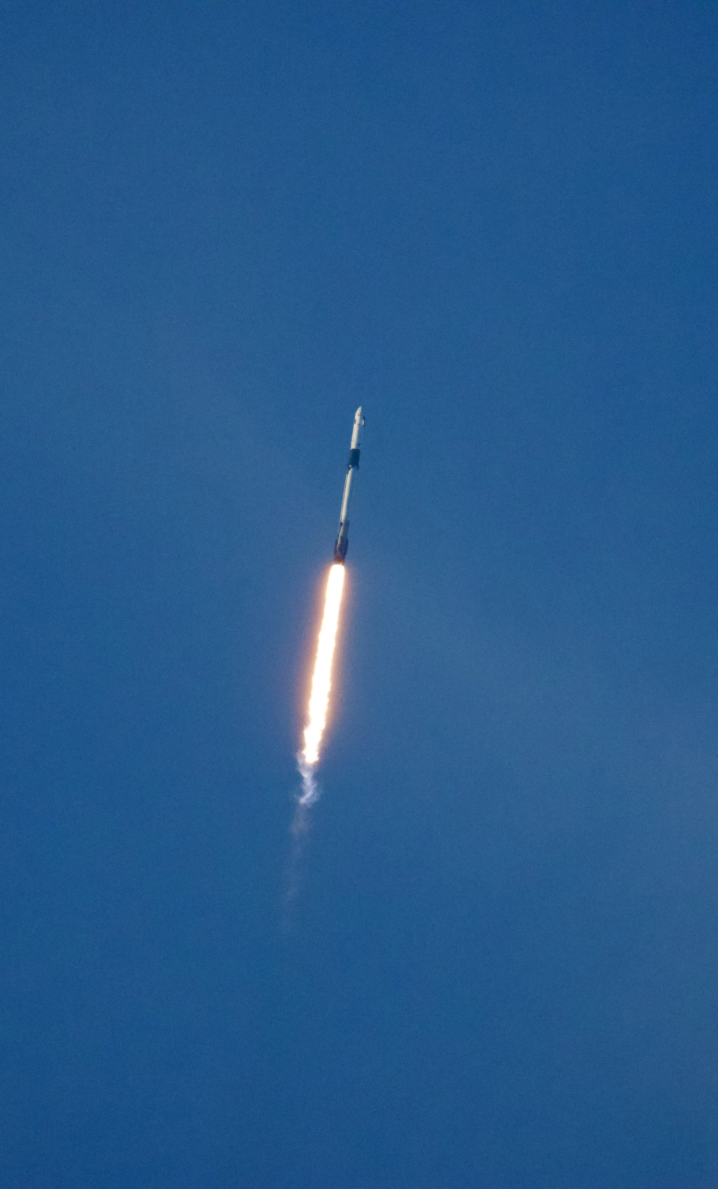 A rocket launching into the sky with a bright trail of flame and smoke against a clear blue sky.