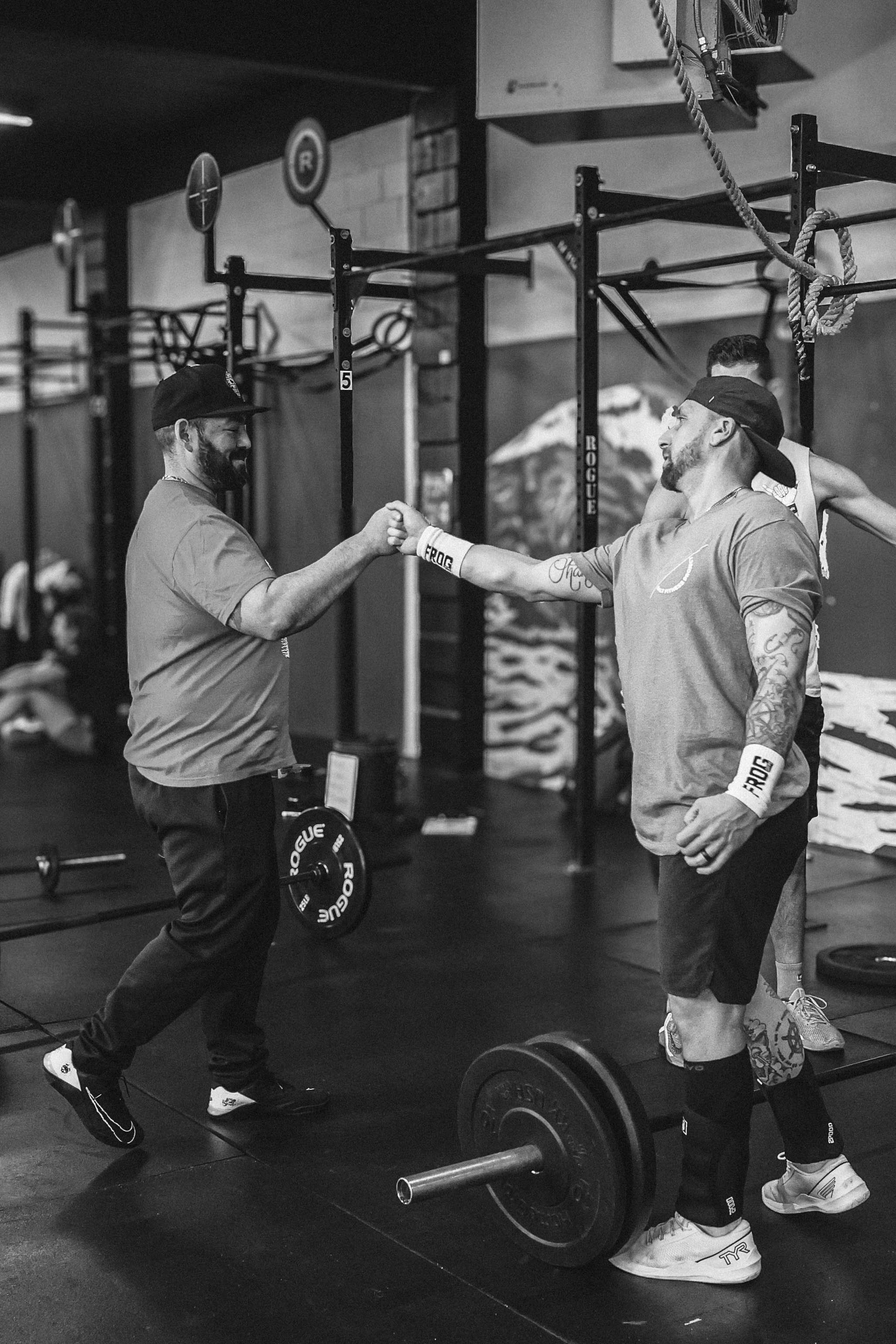 Salt Fitness Project members fist-bumping beside barbells in the gym.