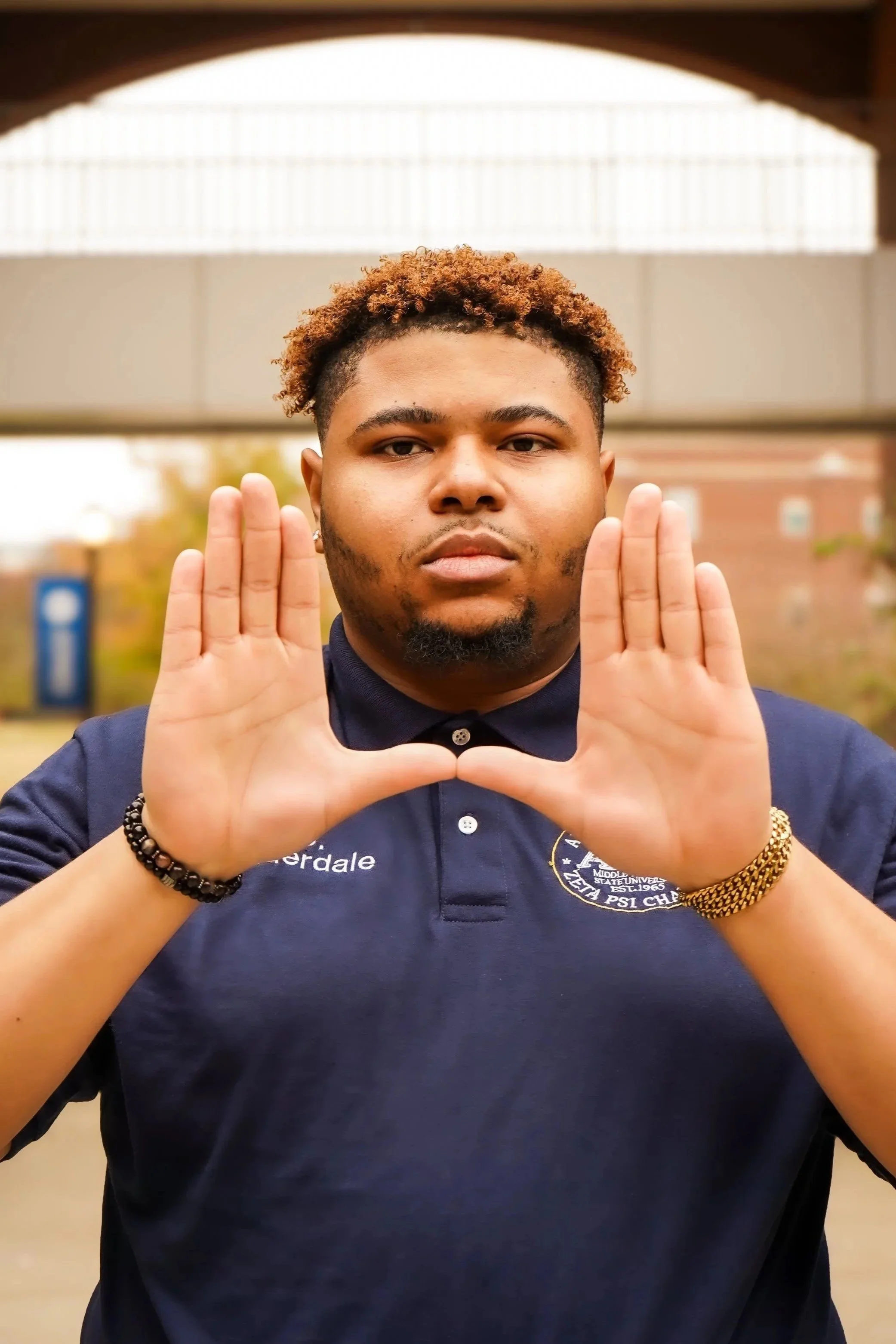 Man wearing a navy blue polo shirt making a "bridge" shape with hands, outdoors.