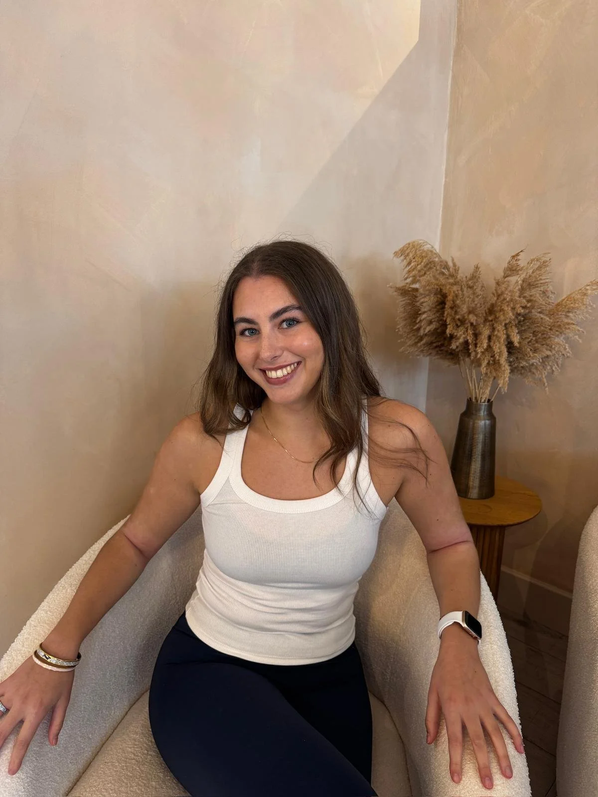 Smiling person with curly hair and glasses wearing a striped shirt and necklace.