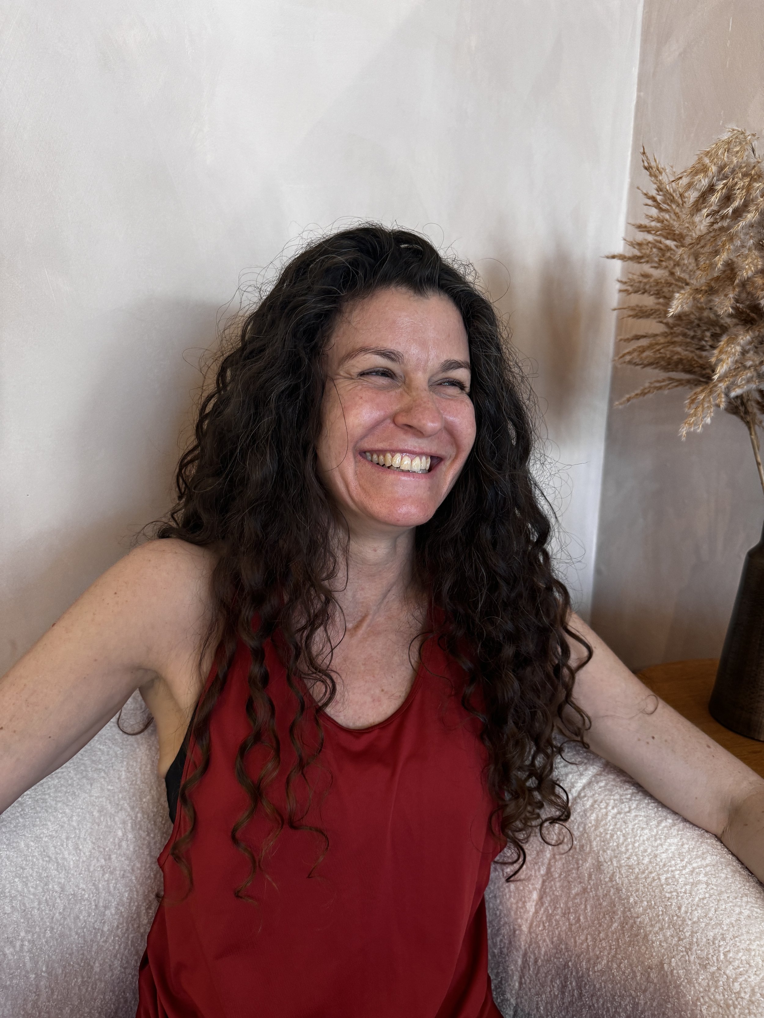 Smiling person with dark hair against a green leafy background.