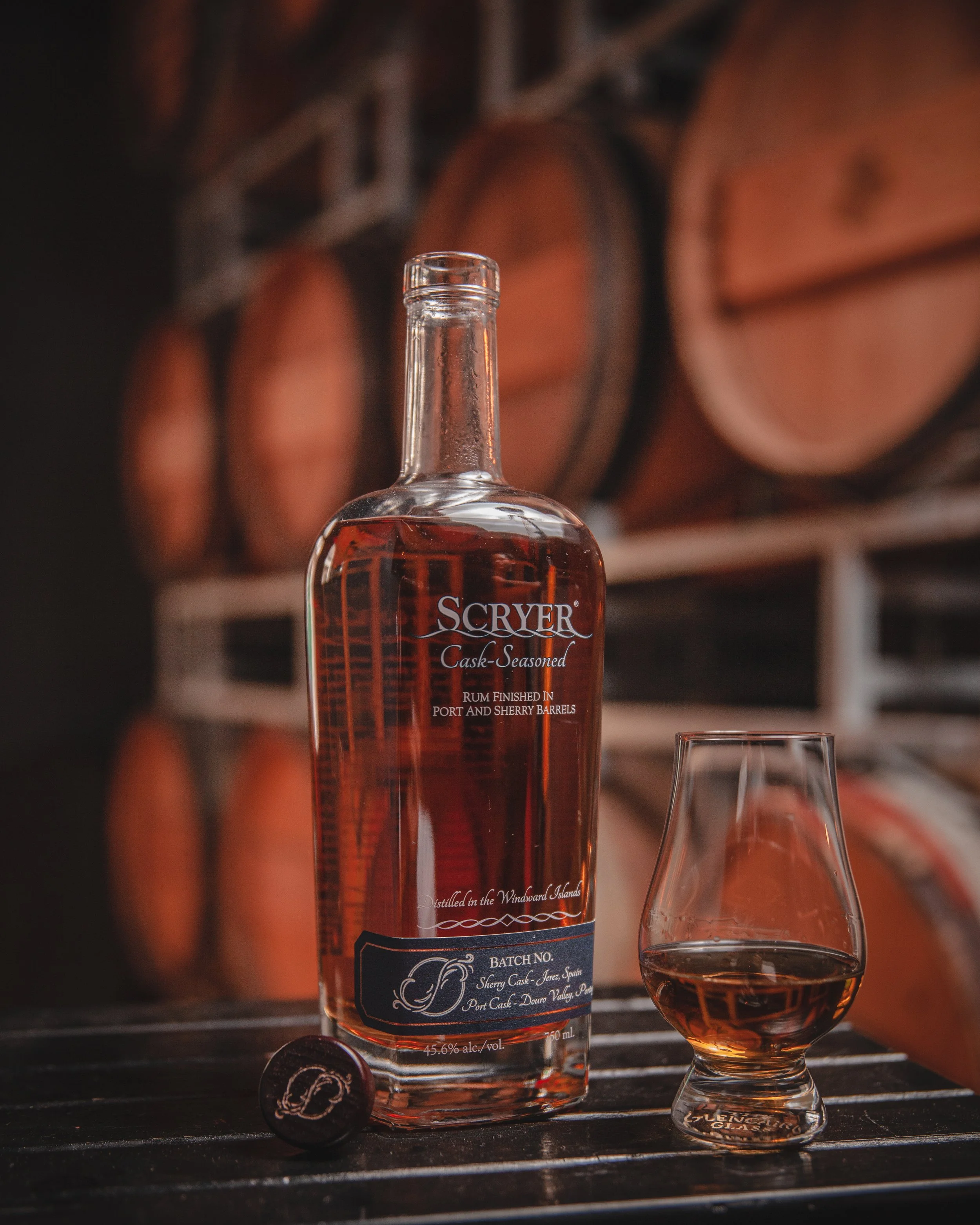 Scryer Rum bottle and glencairn glass in-front of barrels.