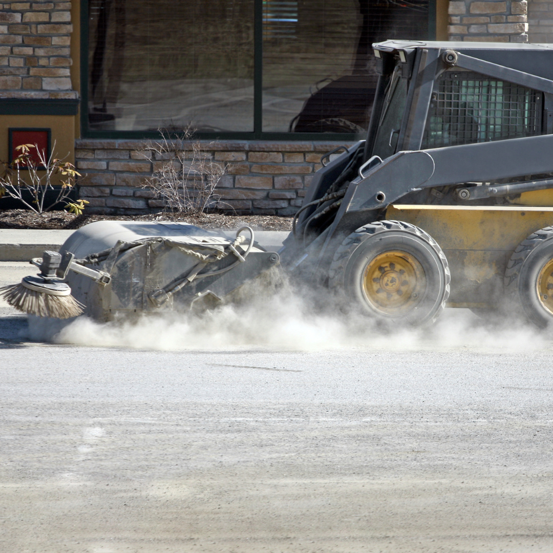 Worker sanding and clearing a parking lot during winter.