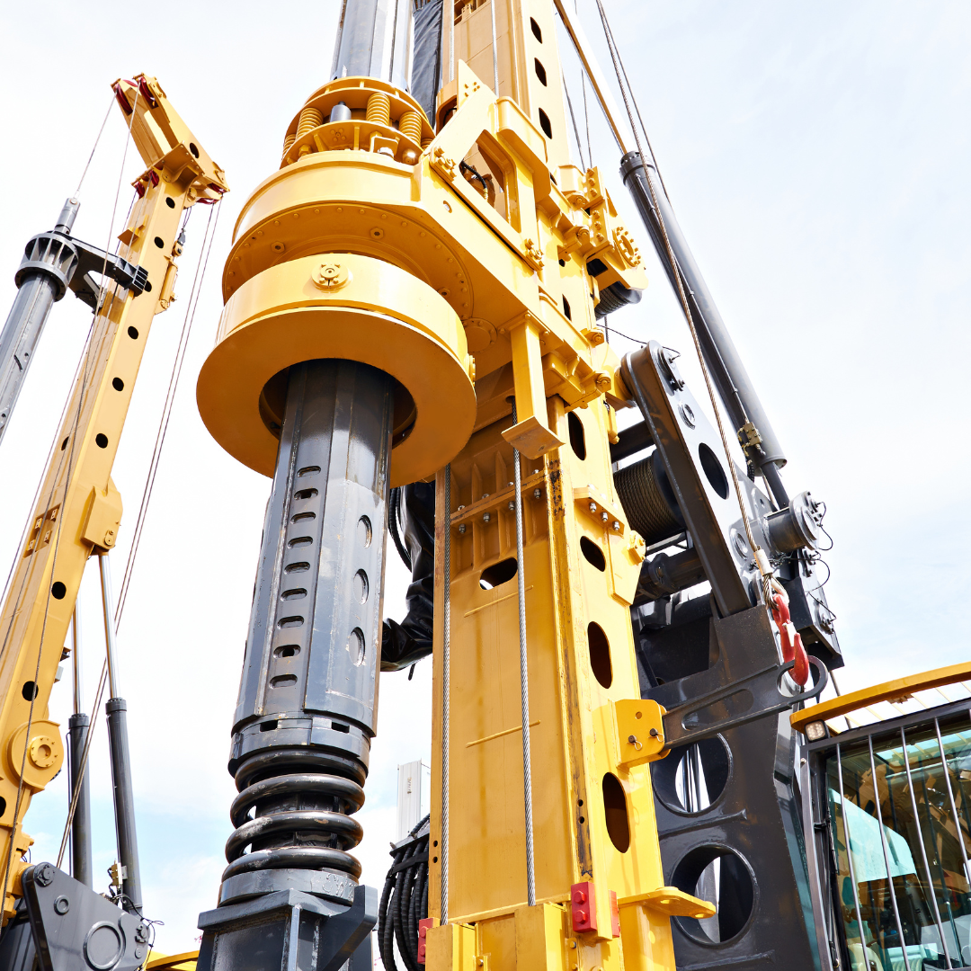 Close-up view of a yellow construction drilling rig with black and metal parts against a cloudy sky.