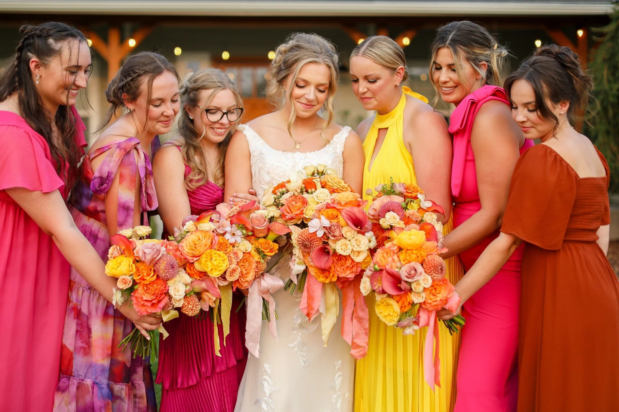 A bride and seven bridesmaids holding bouquets, standing outdoors at a wedding.