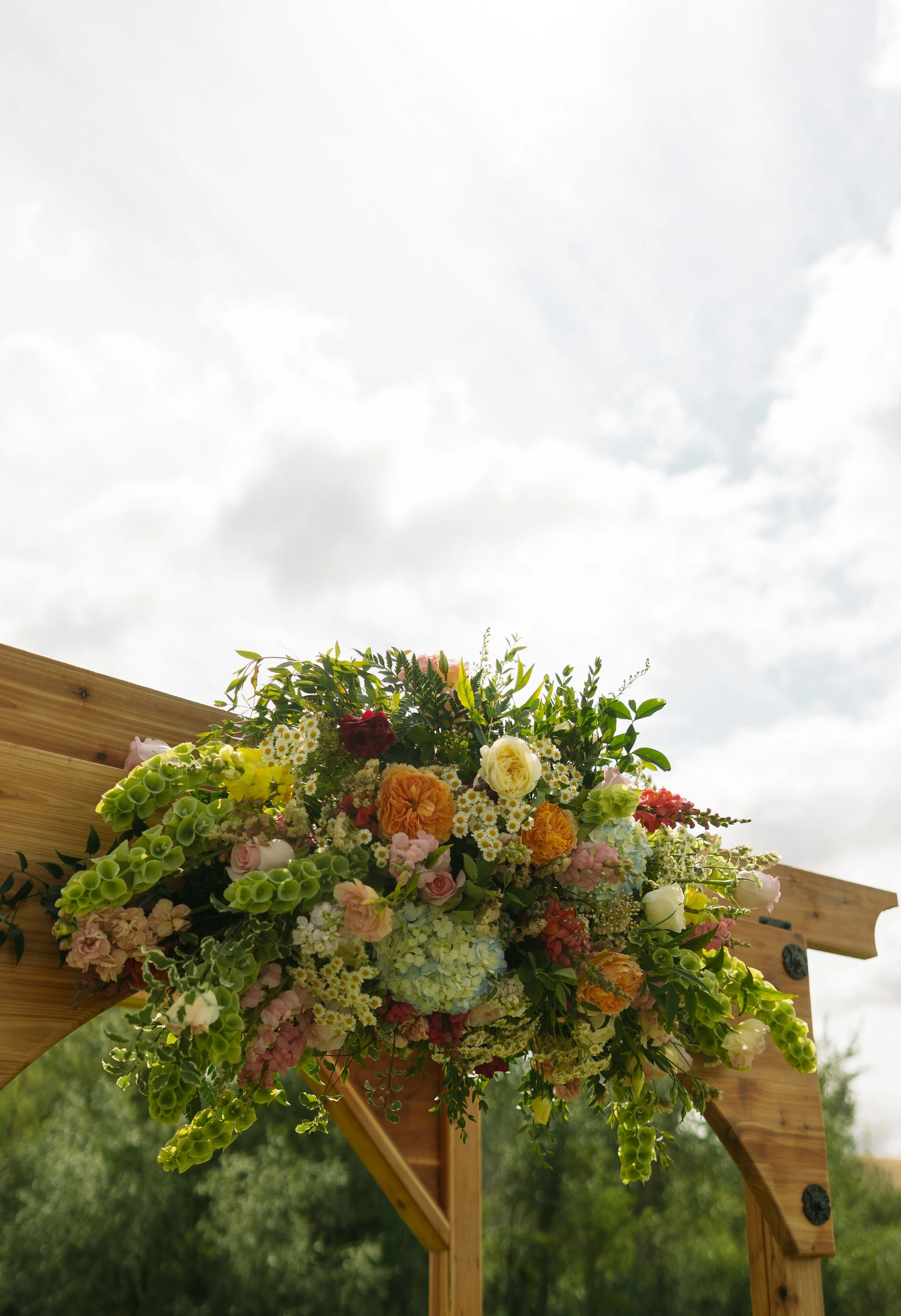 Colorful floral arrangement with various flowers attached to a wooden structure against a cloudy sky.