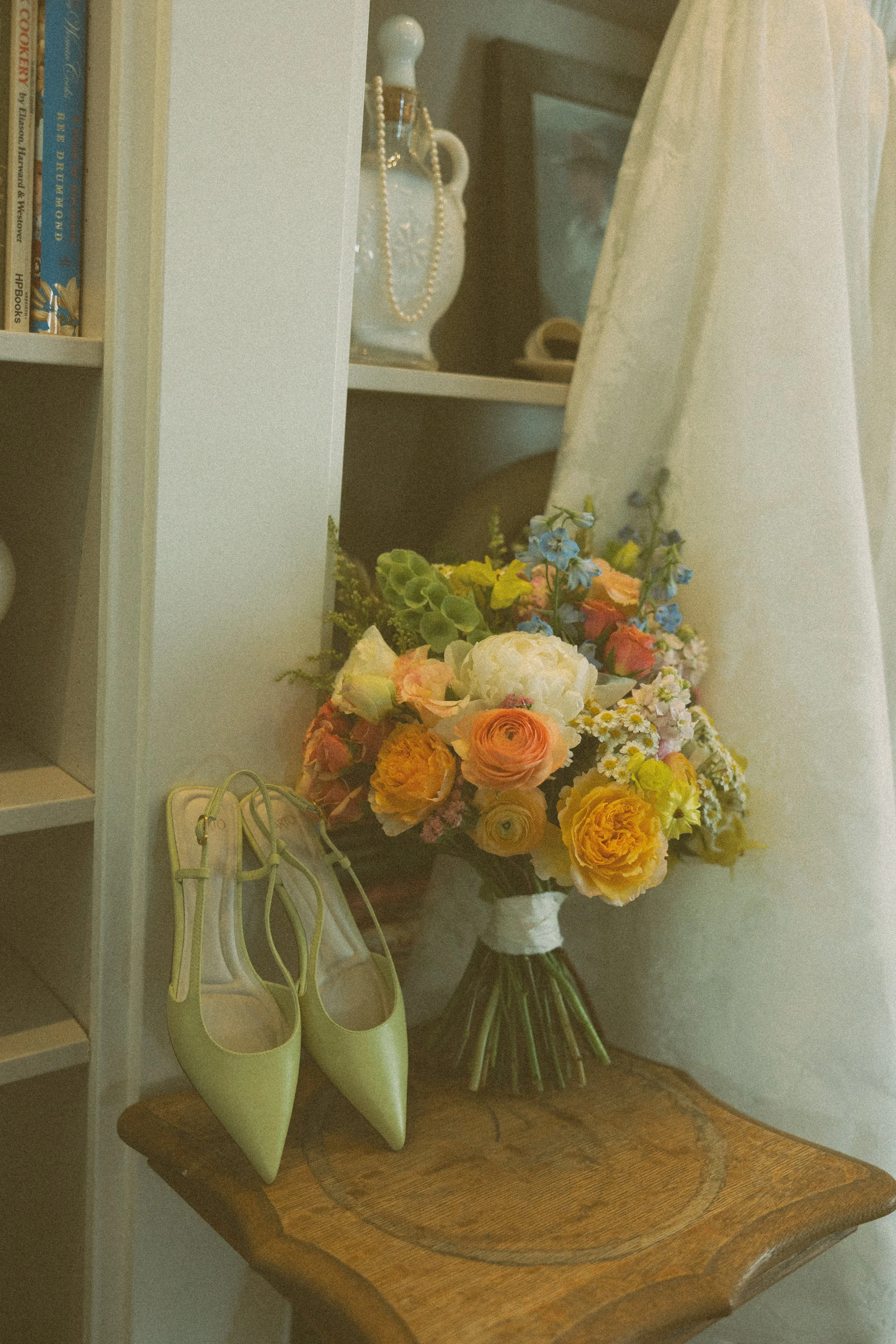 A bouquet of yellow, peach, pink, white, and blue flowers on a wooden table, with a pair of yellow high-heeled shoes beside it.