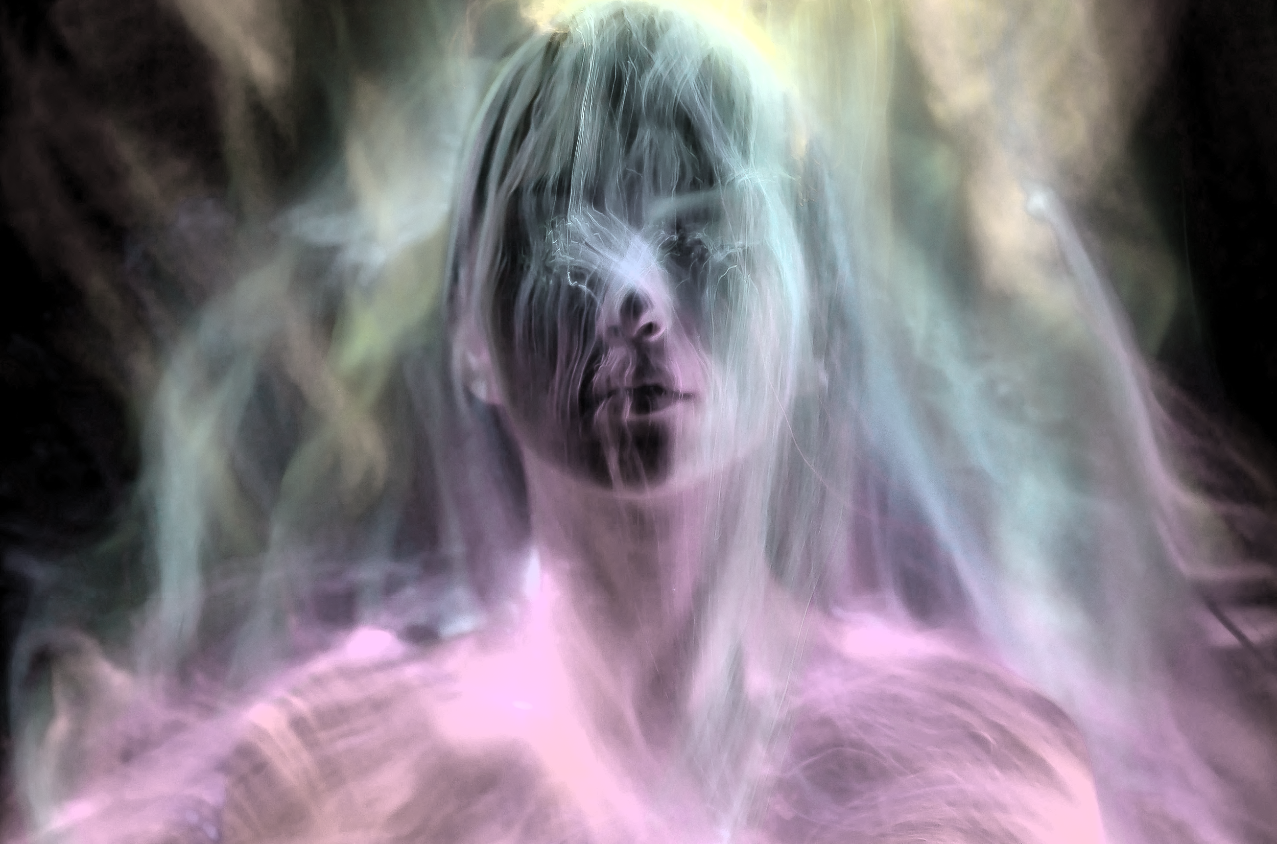 A person with long hair surrounded by colorful, glowing, ethereal mist or energy.