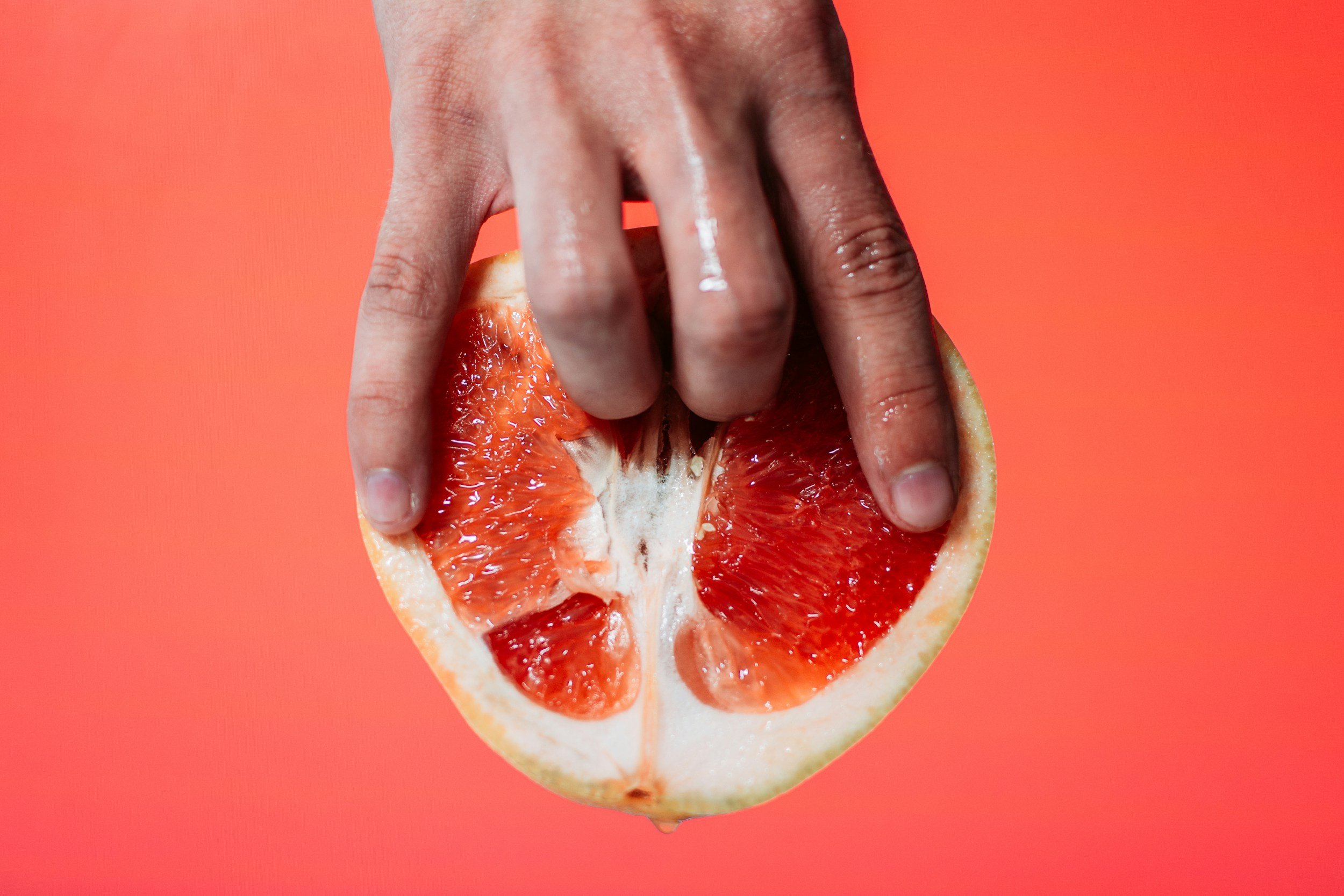 Person holding a halved pink grapefruit against a red background.