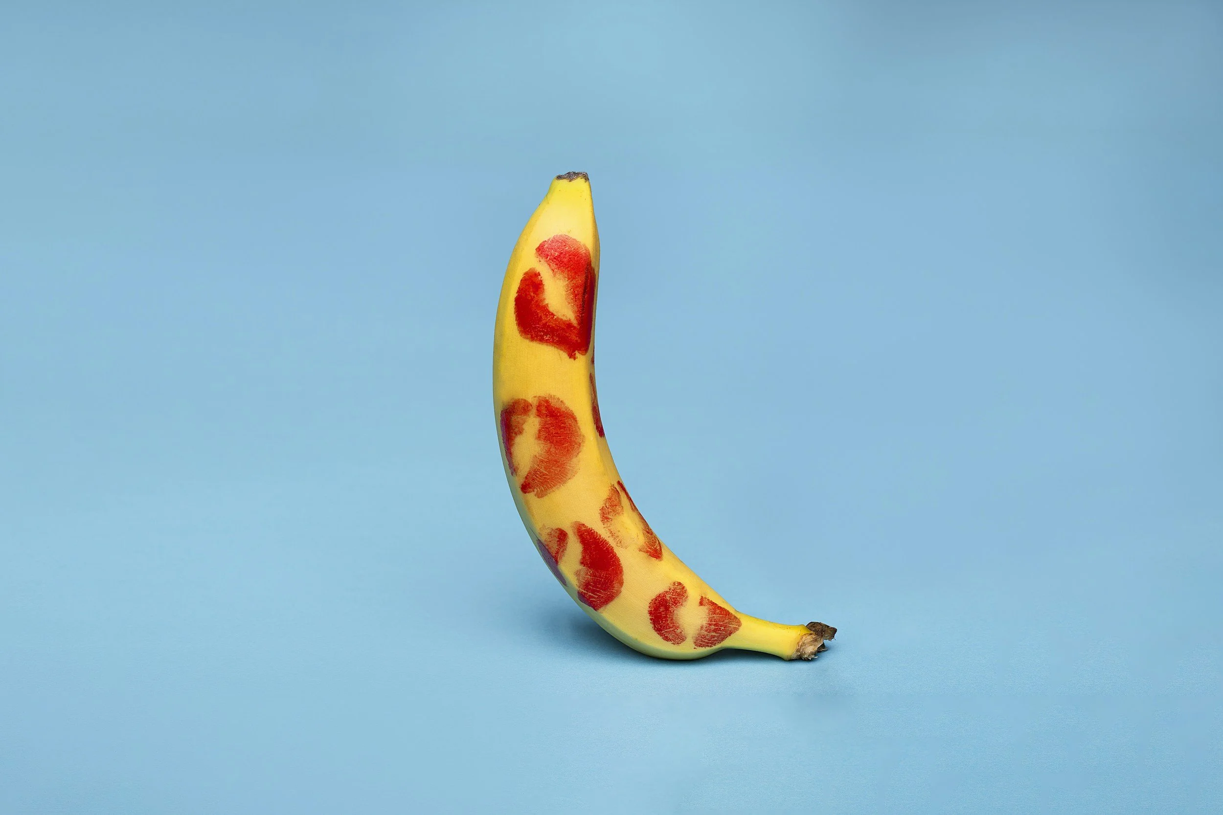 A banana with red lipstick kiss marks on its peel, set against a blue background.