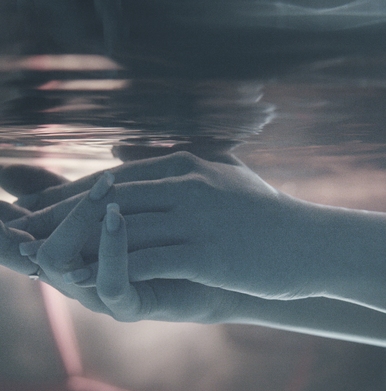 Two hands touching beneath the water surface, with gentle ripples and soft lighting.