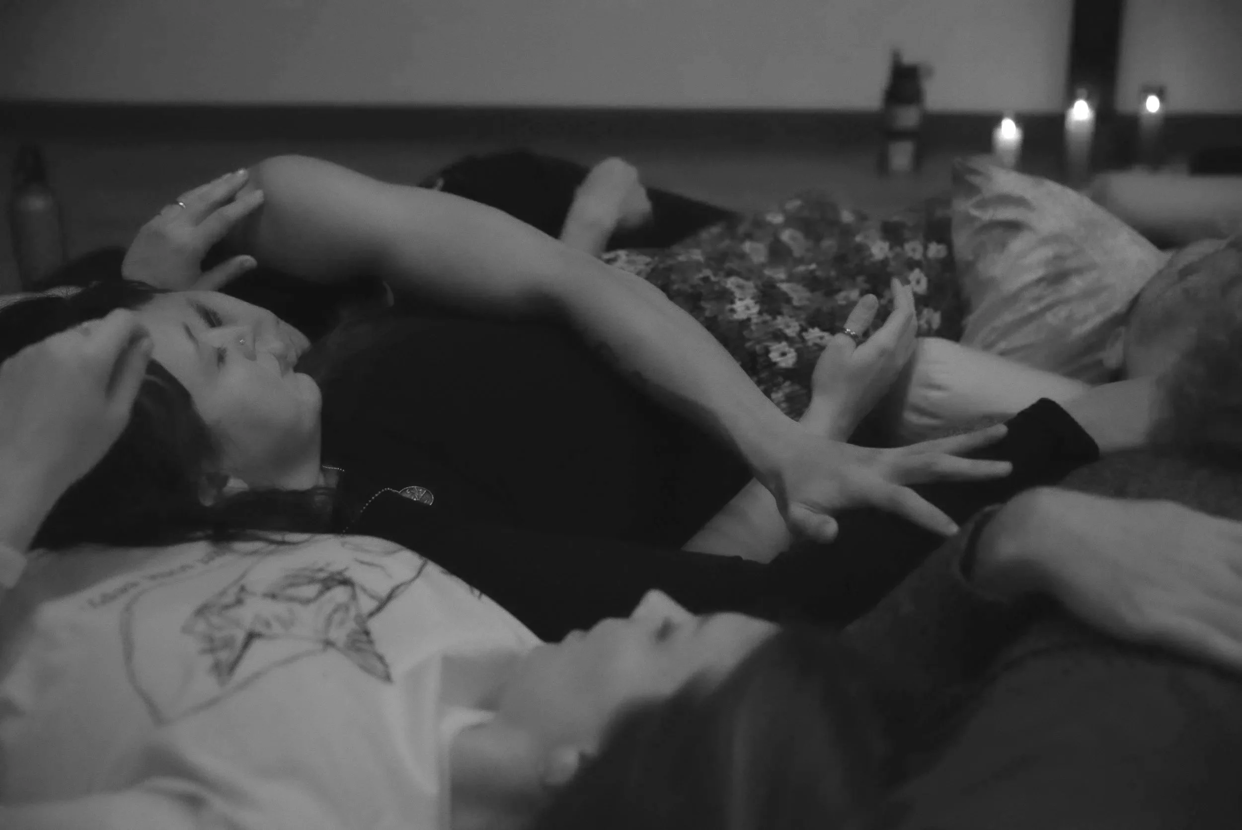 Two people lying on a bed, holding hands, with candles in the background.