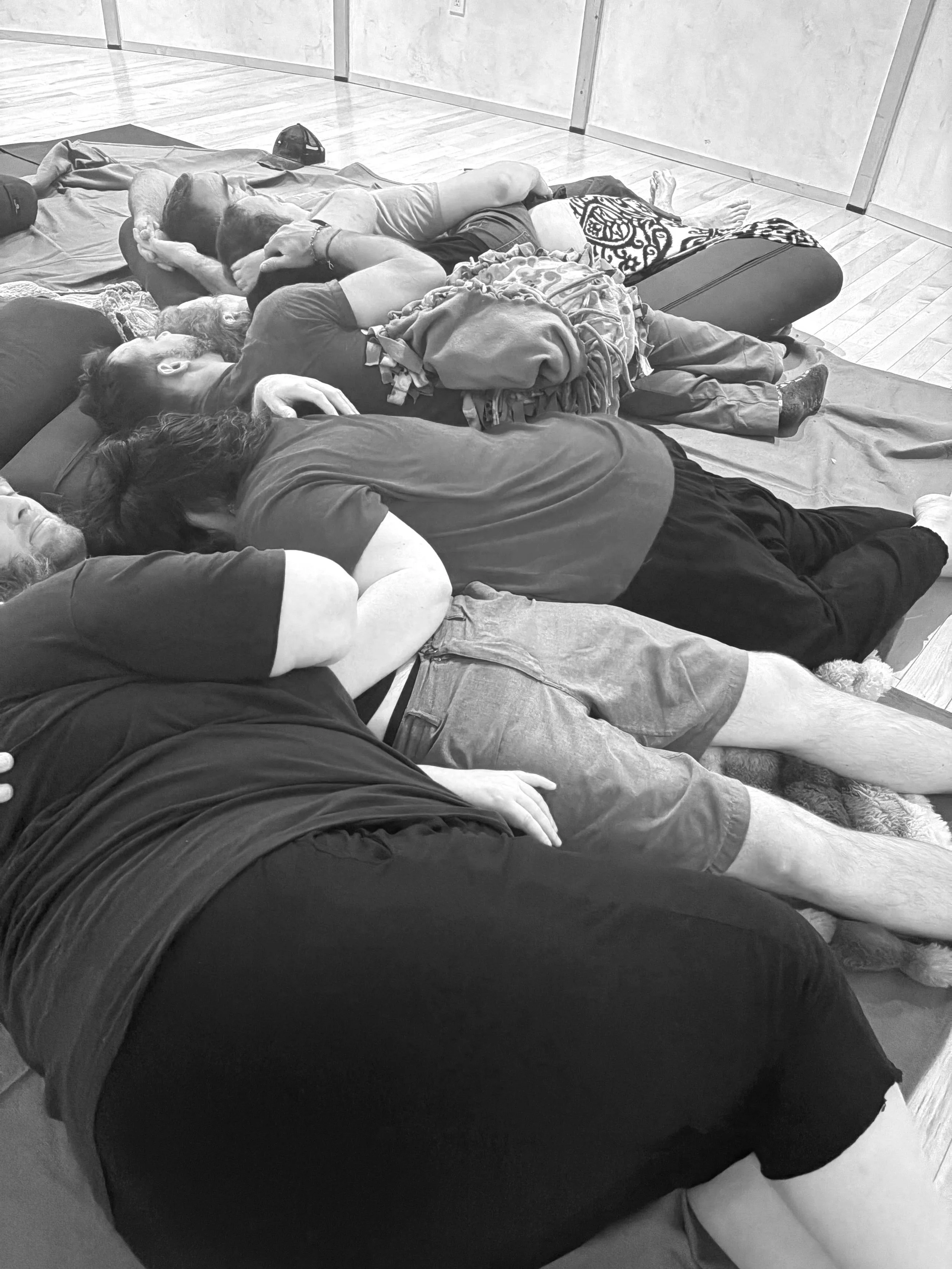 Group of people lying on mats in a room, appearing to be practicing a group relaxation or meditation session.