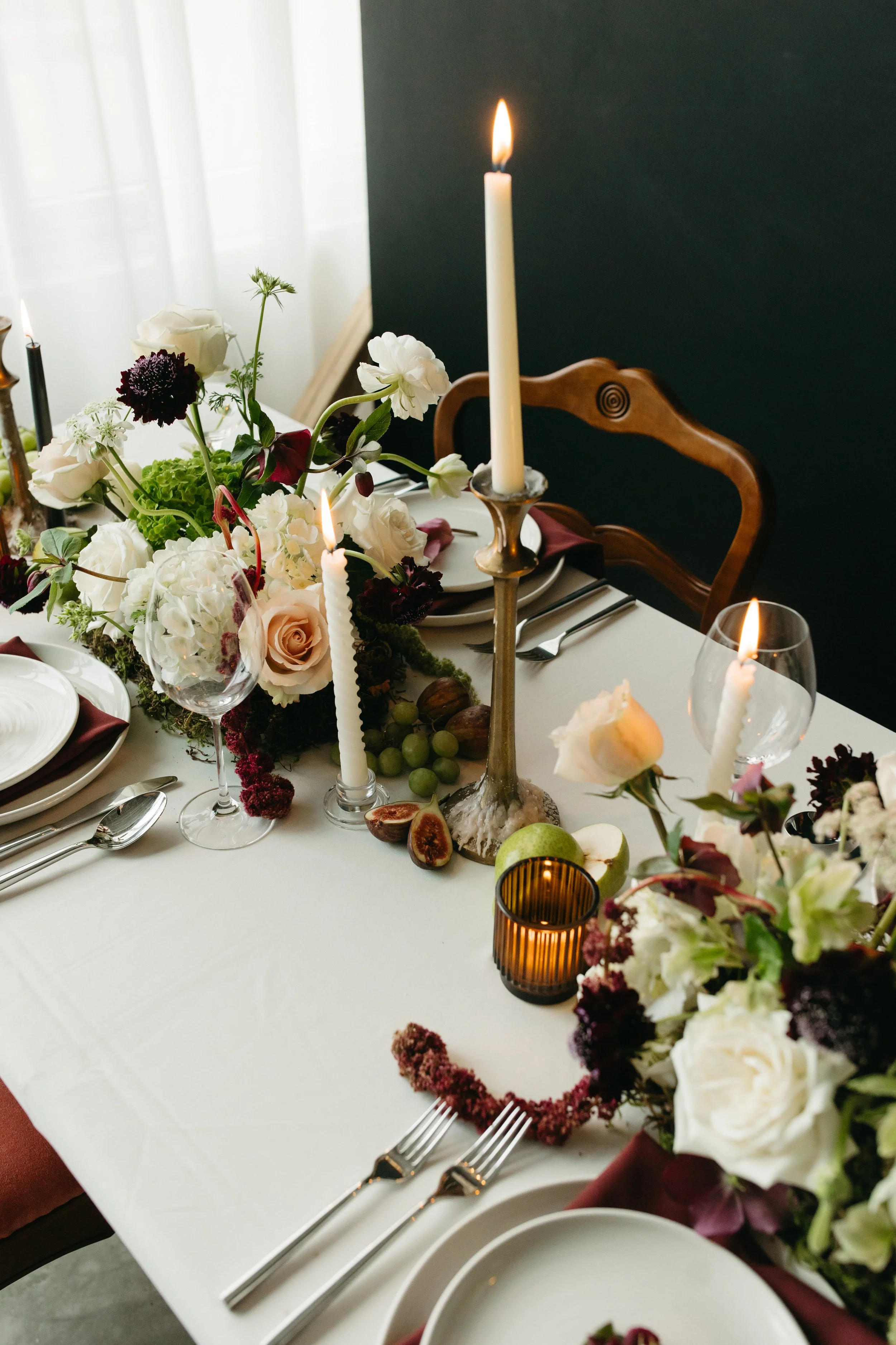 Elegant wedding reception table with low floral centerpieces, lit candles designed in a tablescape with fruits by Calgary's wedding florist Petals & Loam.