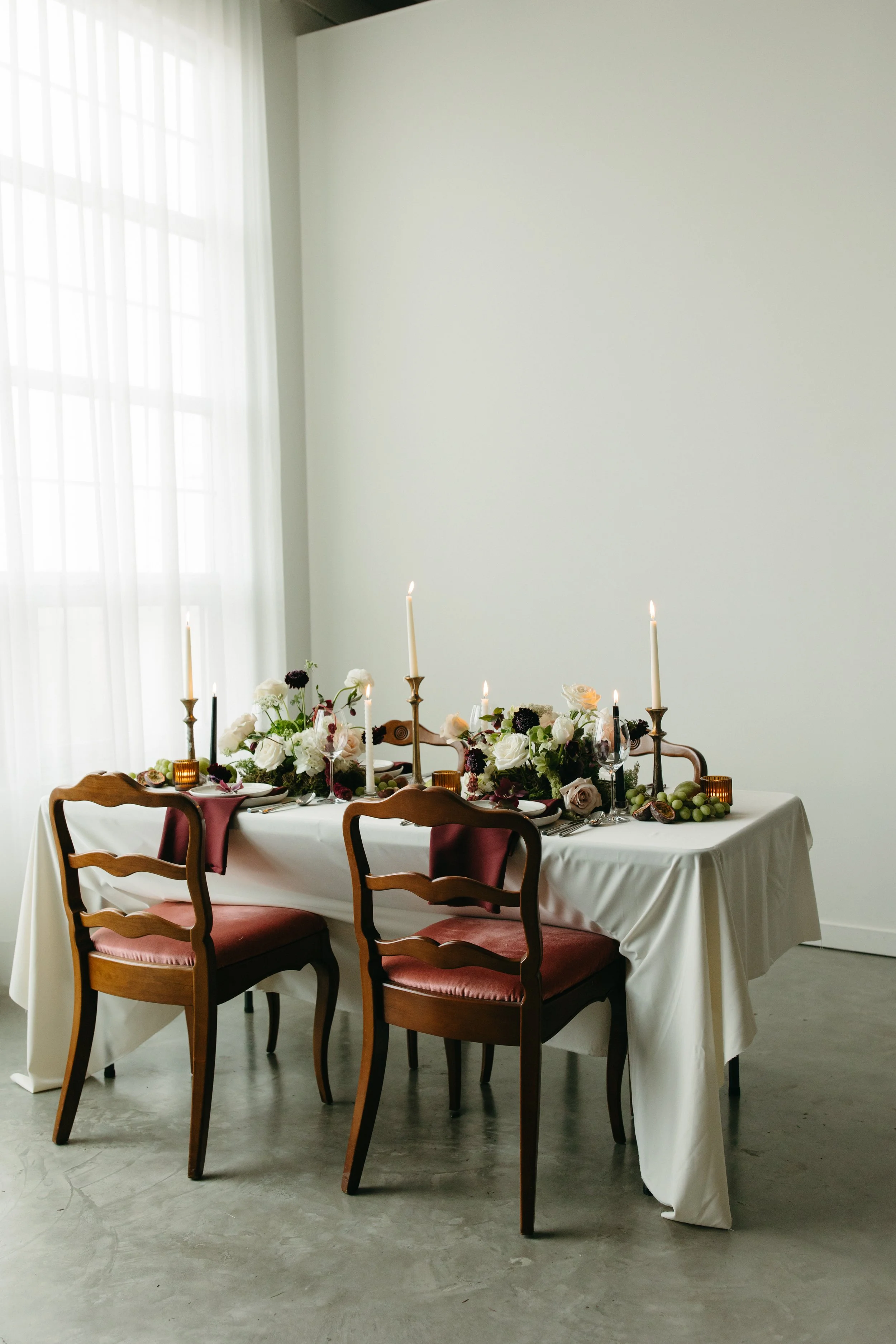 Elegant reception table decorated with low floral centerpiece, tall candles, and dinnerware. Calgary wedding florist Petals & Loam tablescape design.