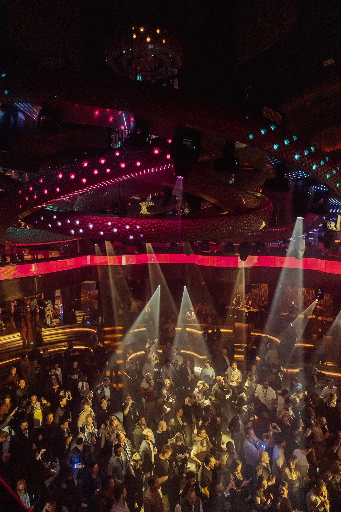 Crowded nightclub dance floor with people dancing, illuminated by stage lights and colorful LED lights on the ceiling and walls.