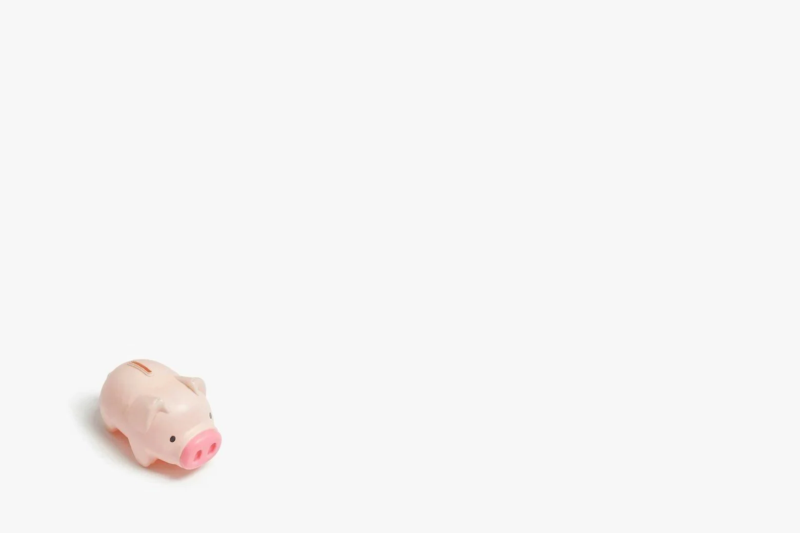 A pink piggy bank lying on a white surface, with a coin slot on its back and a coin on its side.