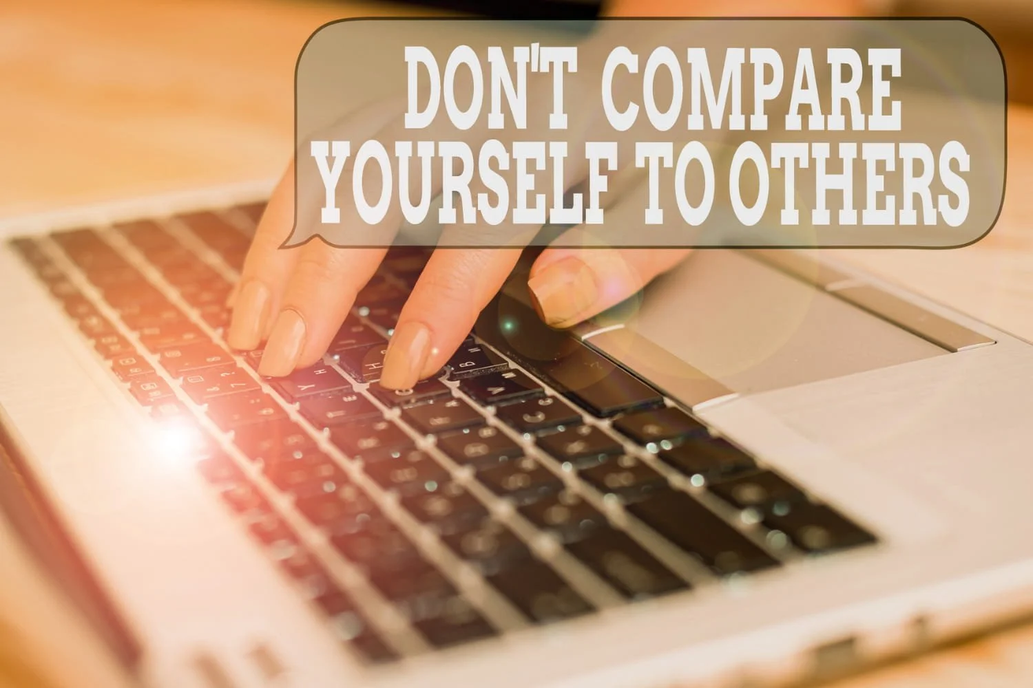 A person's hand on a laptop keyboard with a speech bubble overlay that says don't compare yourself to others.