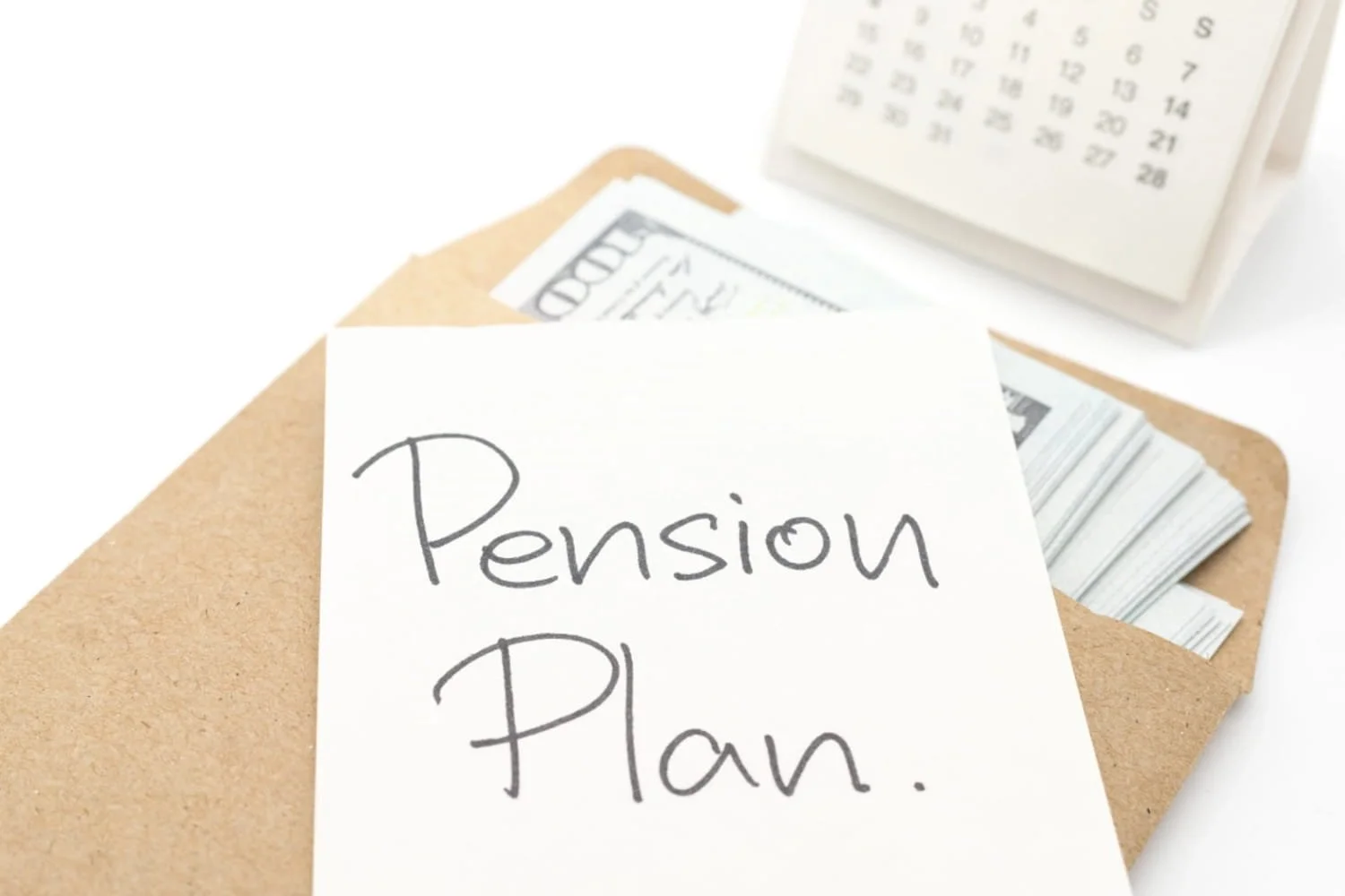 A calendar next to an envelope filled with money and a sticky note on top of the envelope that says pension plan.