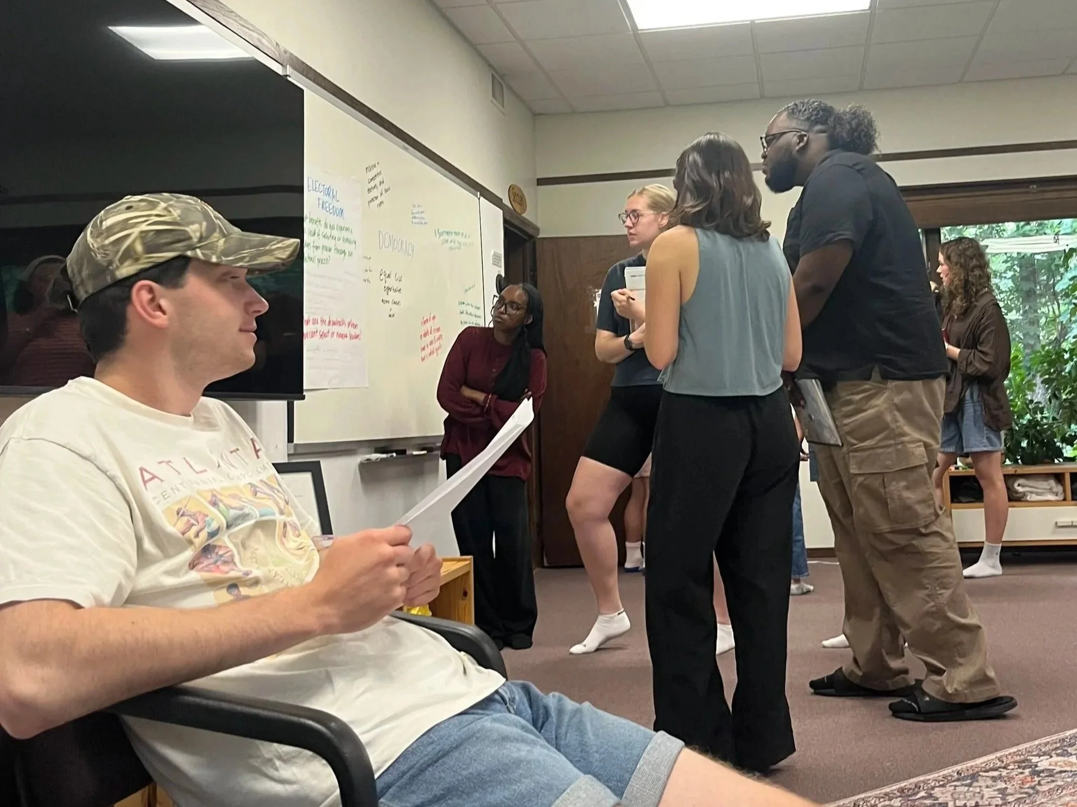 A small group of fellows huddles around a whiteboard, brainstorming ideas related to democracy and its benefits.