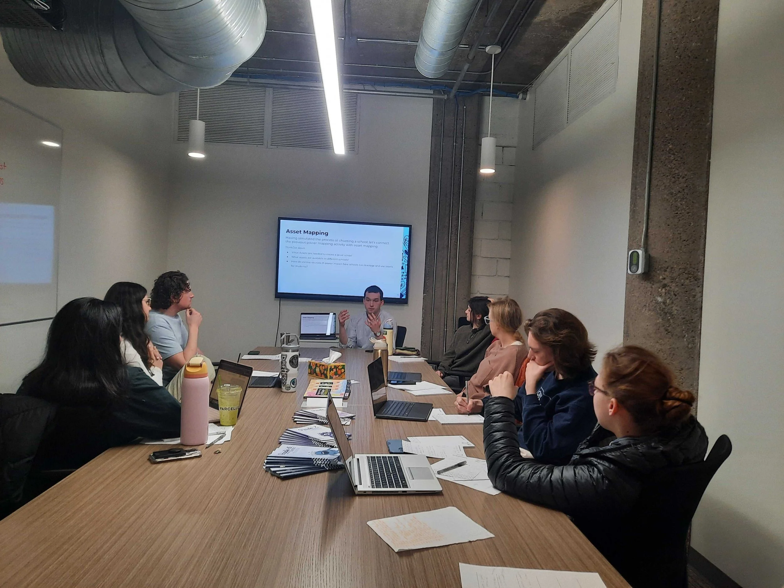 Civic Bridgers Fellow George Lefkowicz addresses the 2025-2026 fellowship cohort. They sit around a rectangular table. A presentation screen is visible in the background.