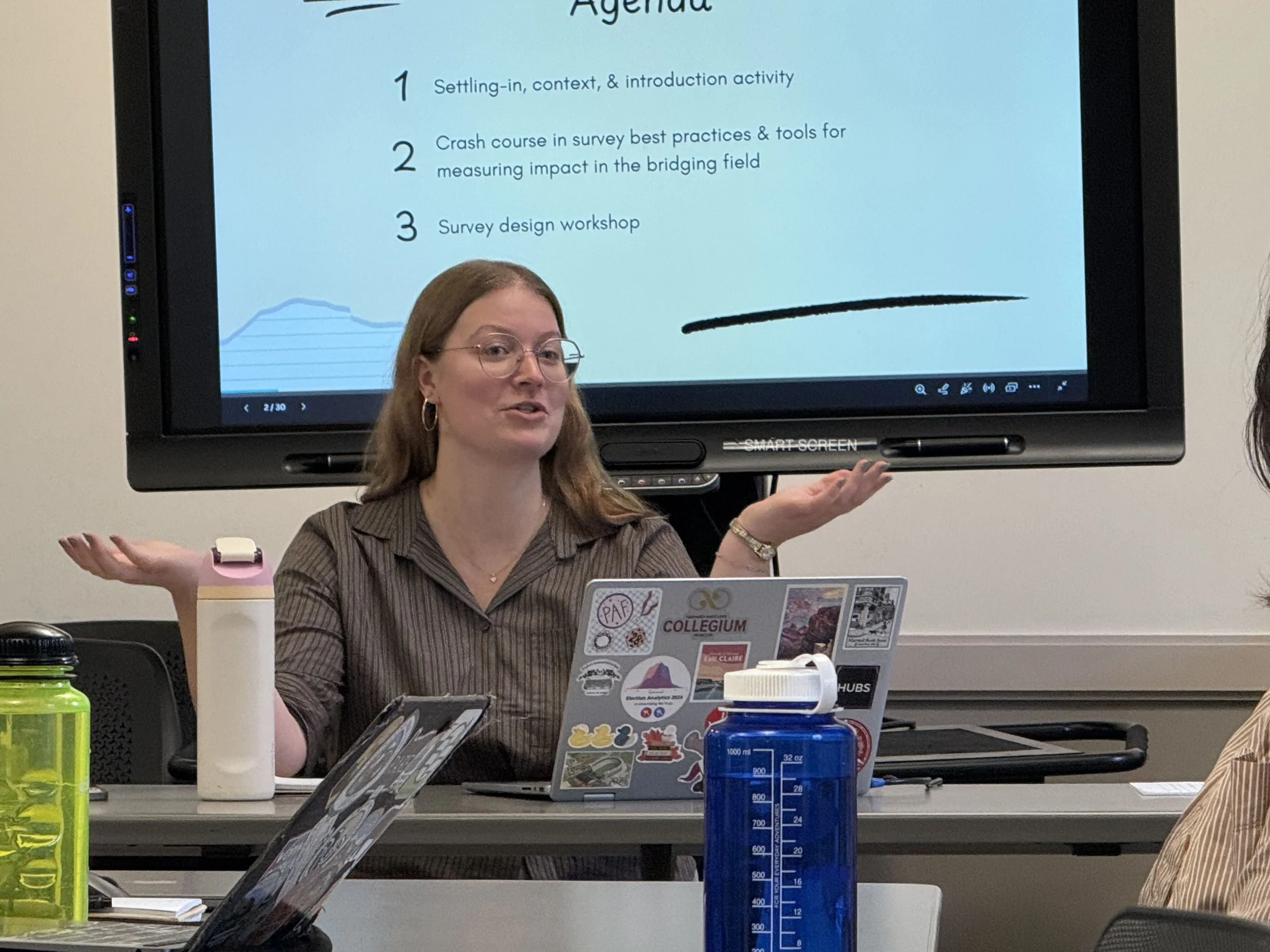 Civic Bridgers Fellow, Alex Heuss, sits at the front of the room presenting the agenda for the day.