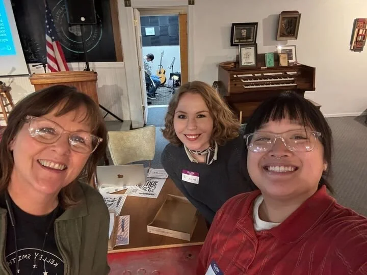 3 people smile for a selfie. a piano and an American flag are visible in the background.