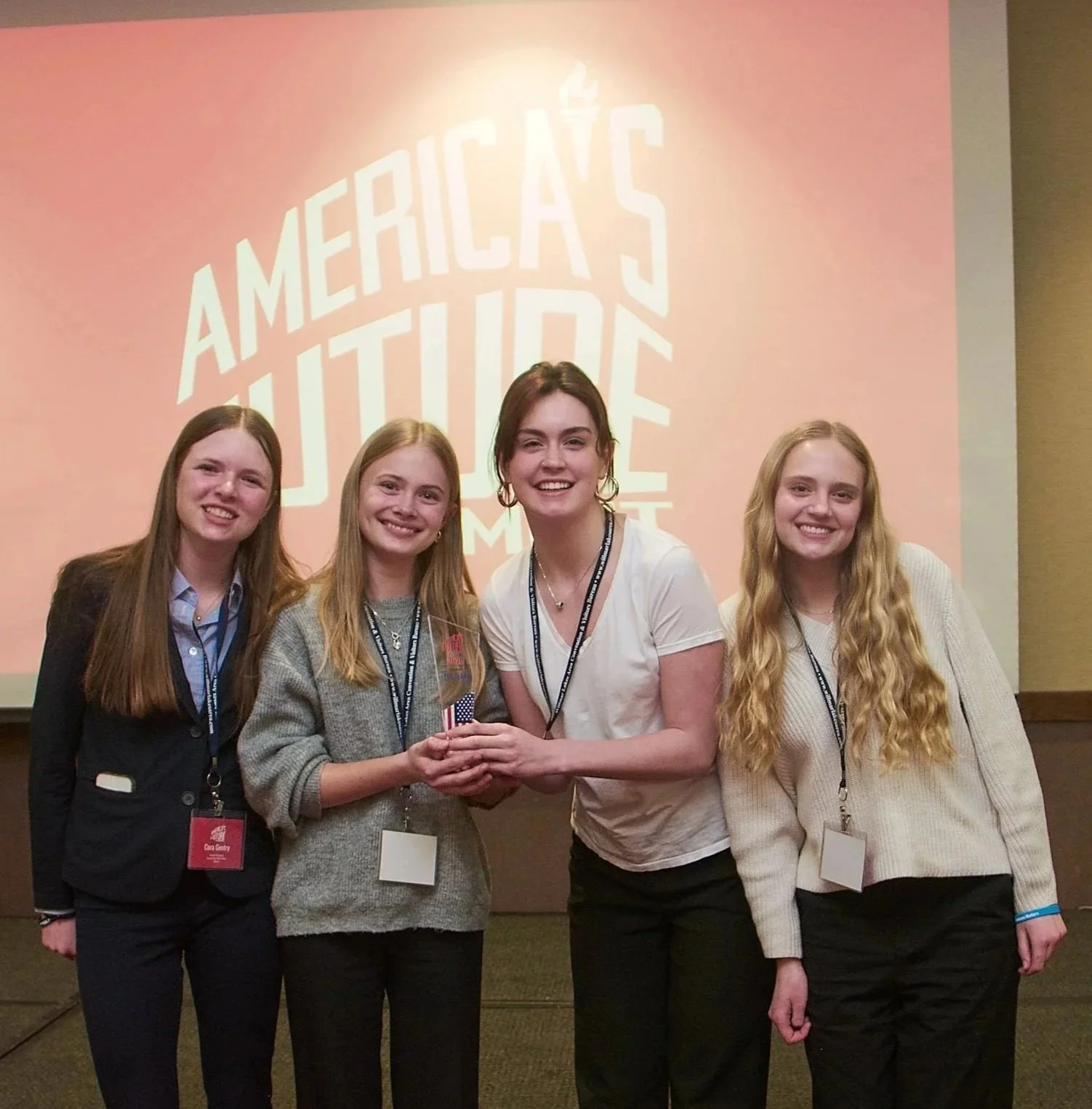 4 young women smile at the camera, holding a glass trophy.