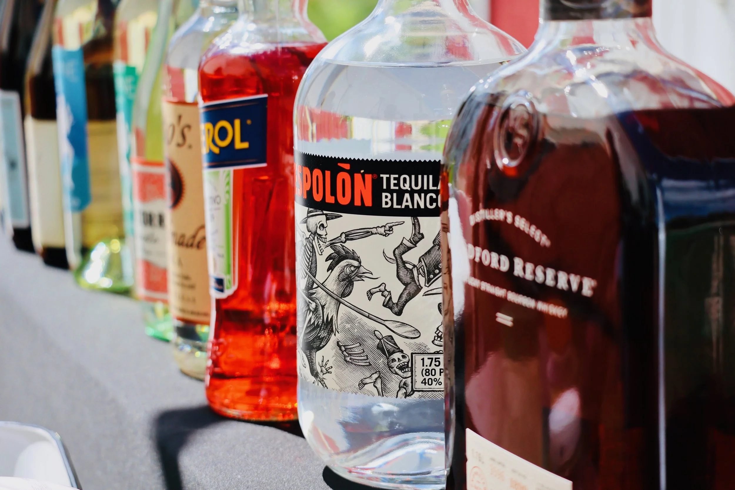 Bottles of alcohol on a shelf, with a clear bottle of Tequila in the foreground, labeled 'Tequila Blanco'.