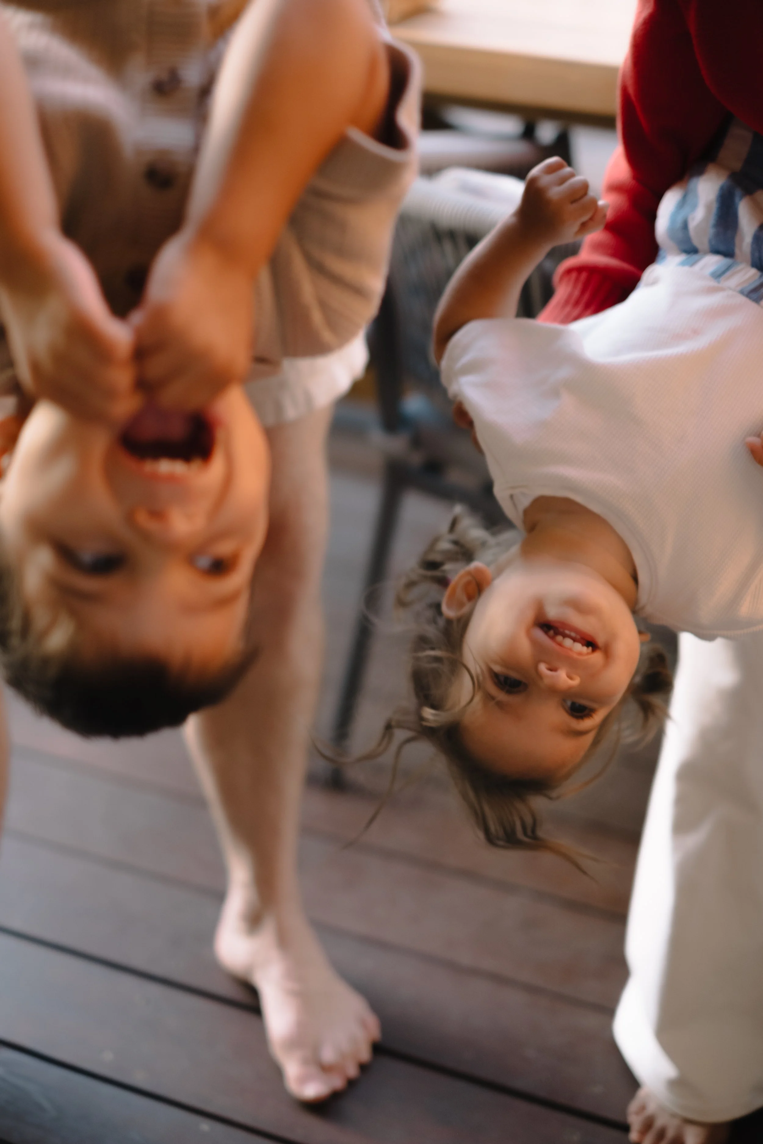 Two young children, a boy and a girl, are playing and smiling, with the boy holding his nose and the girl upside down, both appearing joyful.