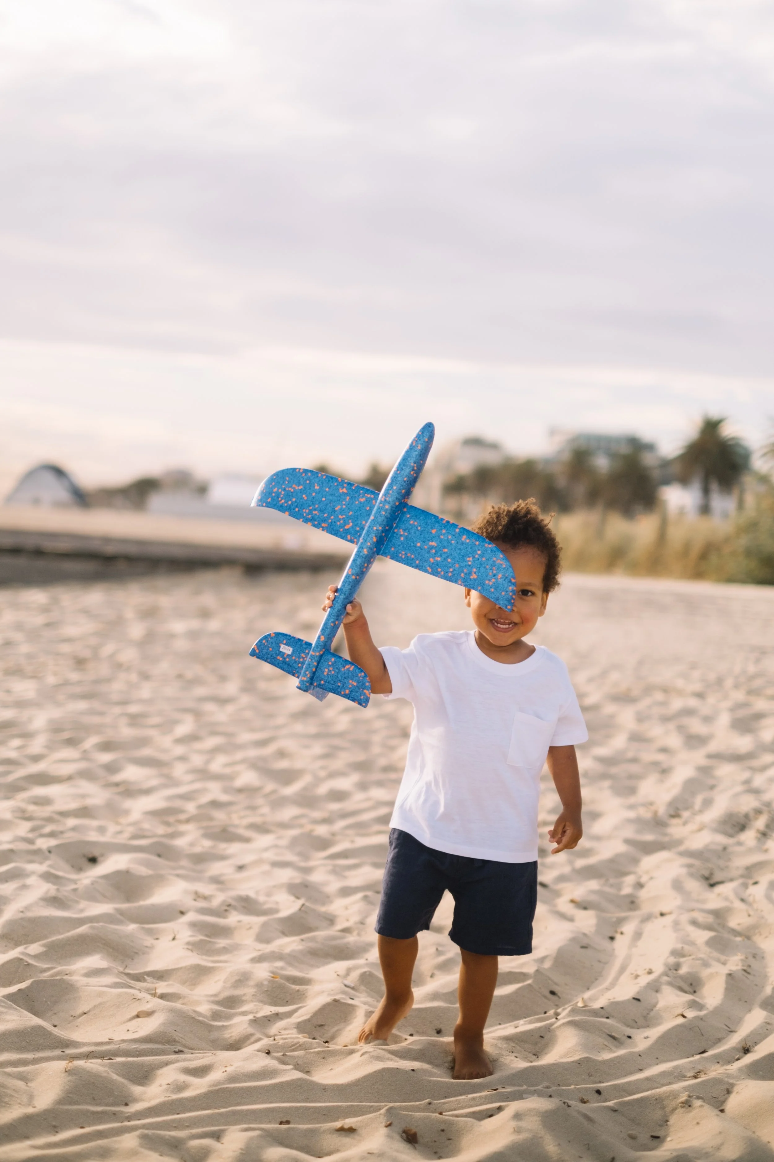 Young child playing on the beach holding a foam airplane.