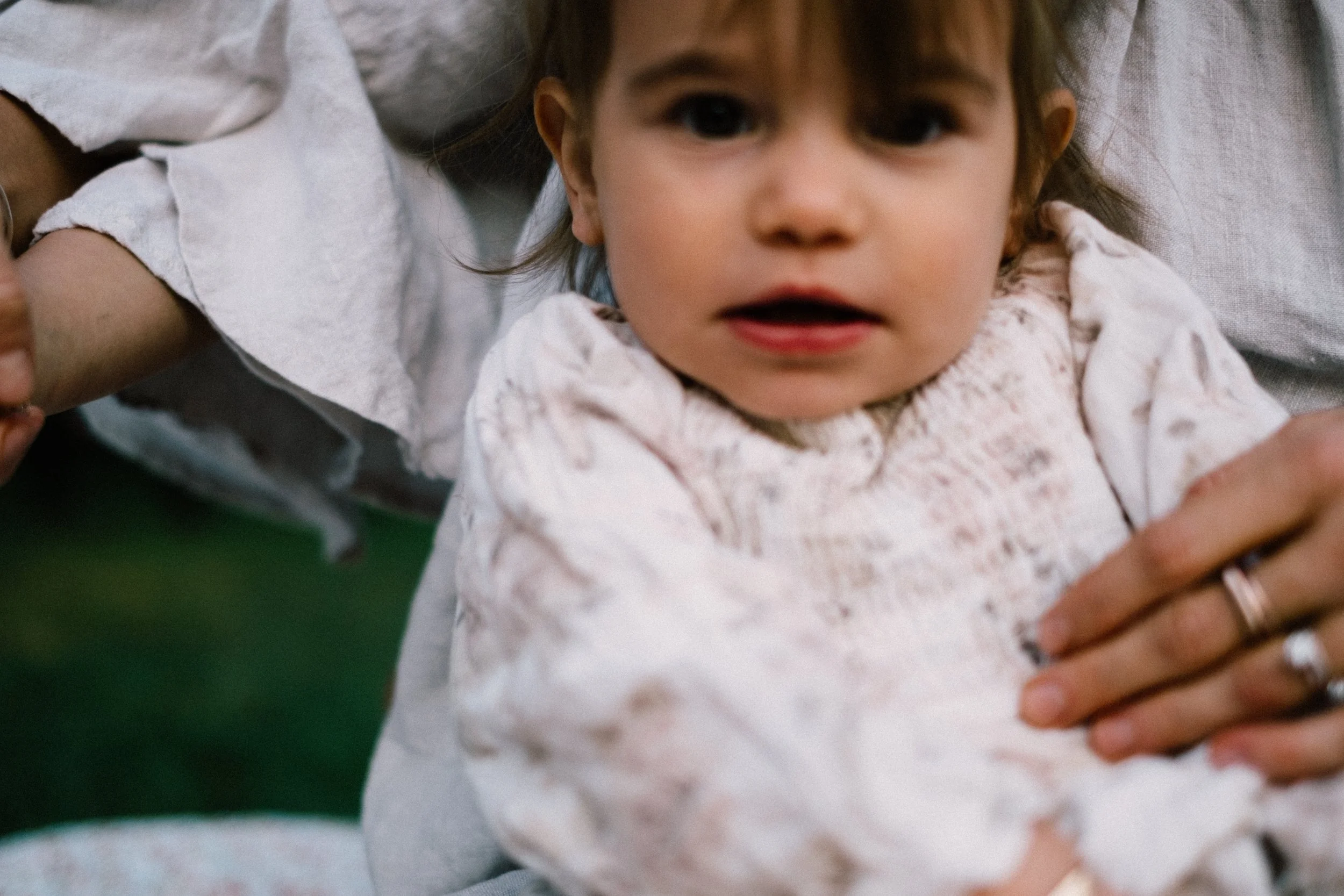 Close-up of a young girl with brown hair and dark eyes, wearing a white blouse, being held by an adult.