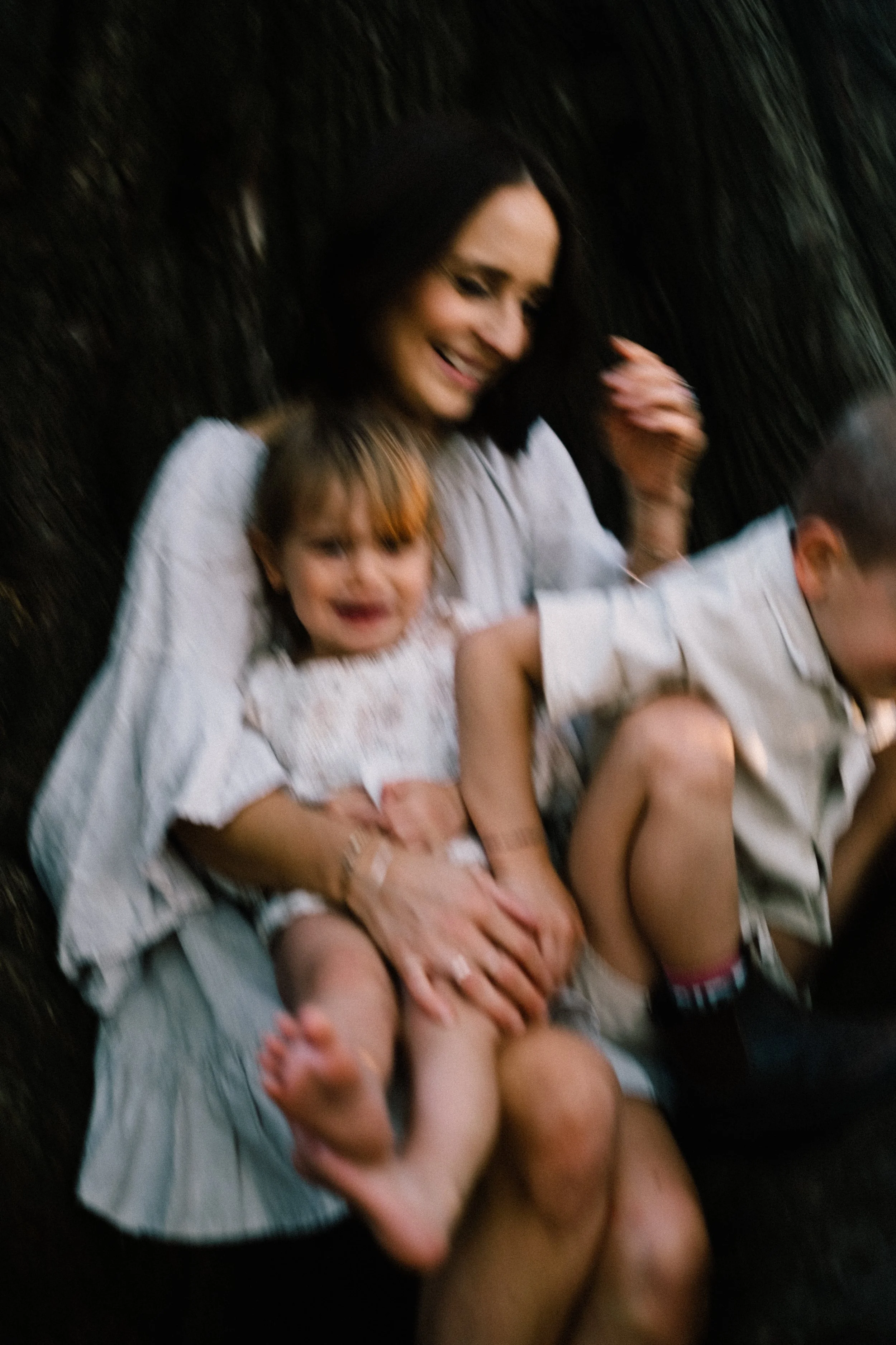 A woman and two children sitting together outdoors, smiling and laughing.