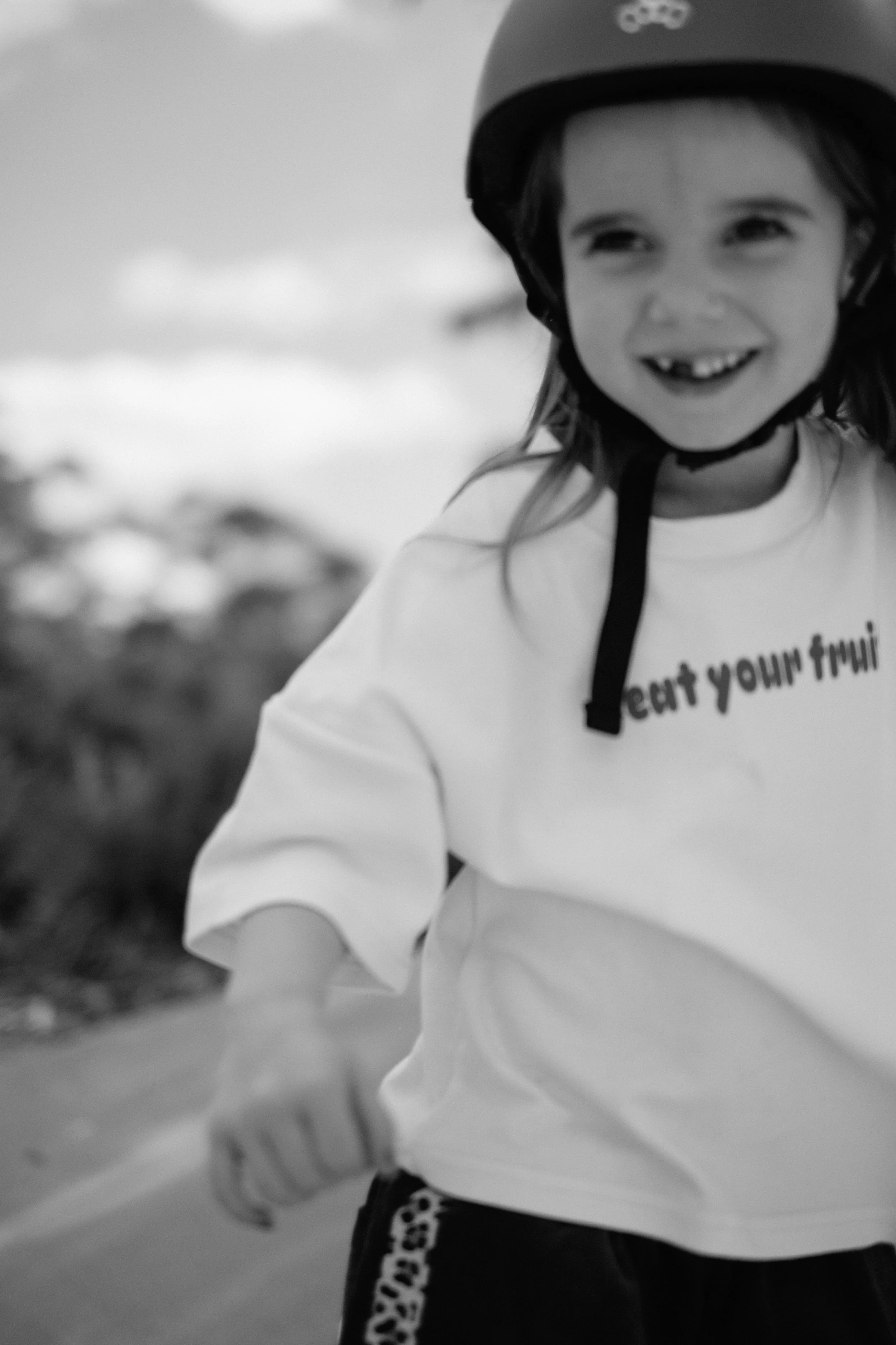 A smiling young girl wearing a helmet and casual clothes, riding a bike outdoors.
