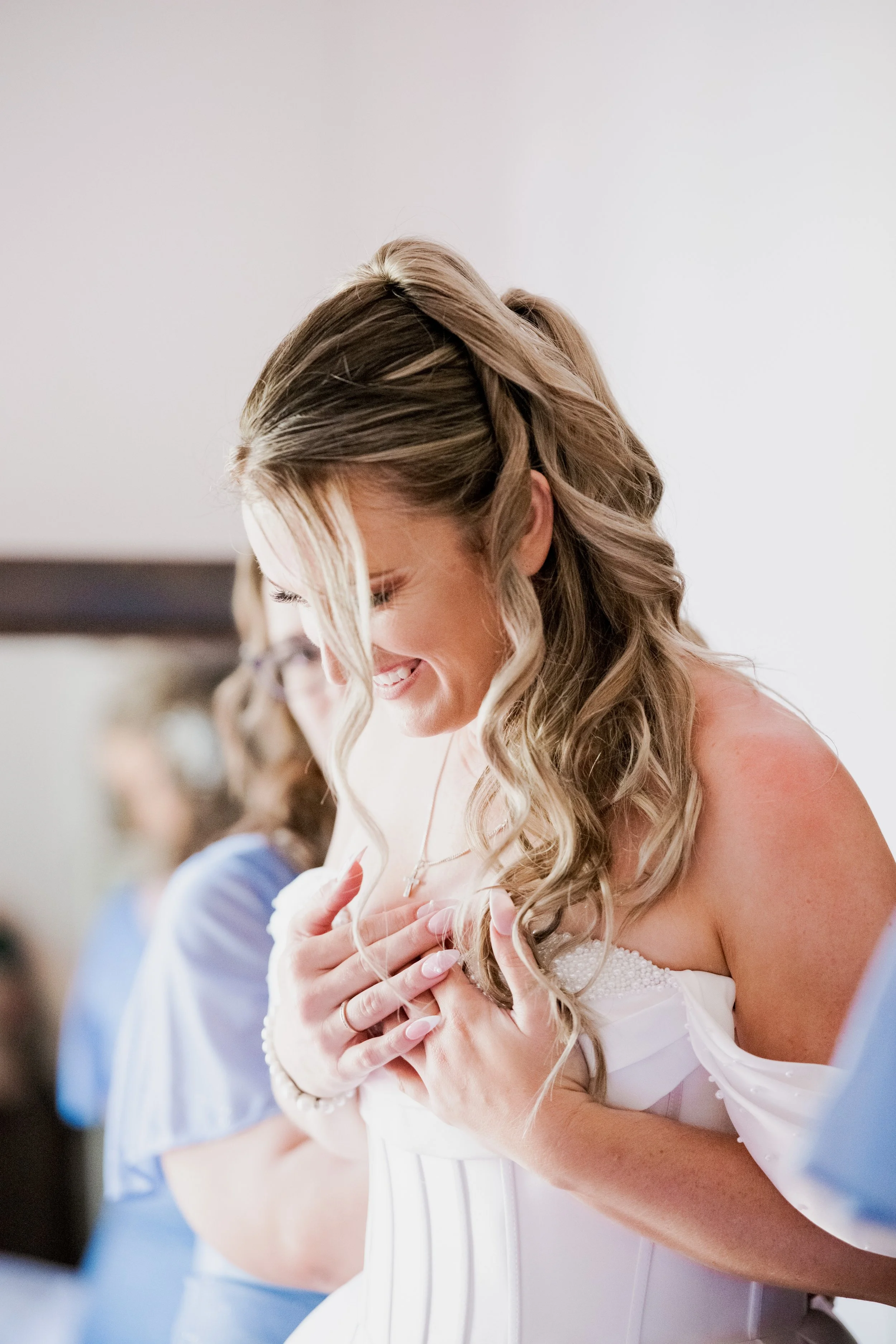 A woman smiling with hands on her chest, in a white dress, possibly a bride, in a joyful moment.