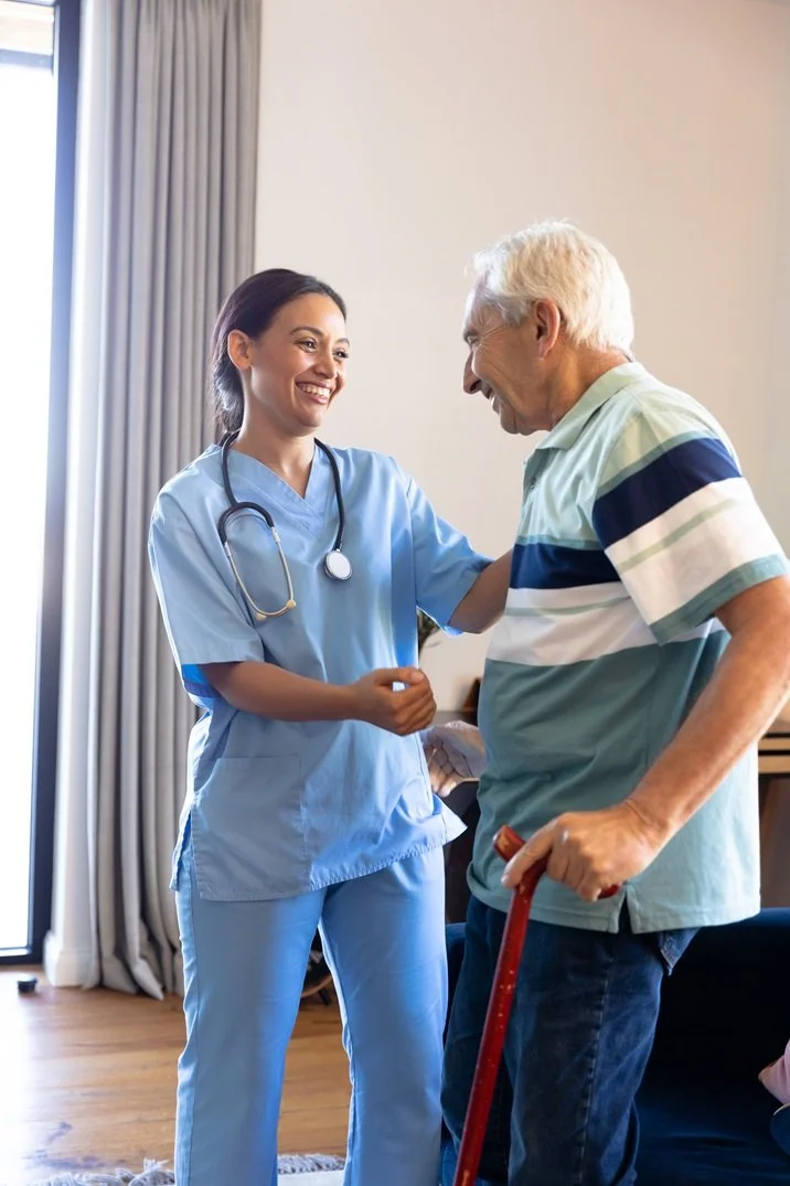 Healthcare professional in blue scrubs assisting an elderly man with a cane.
